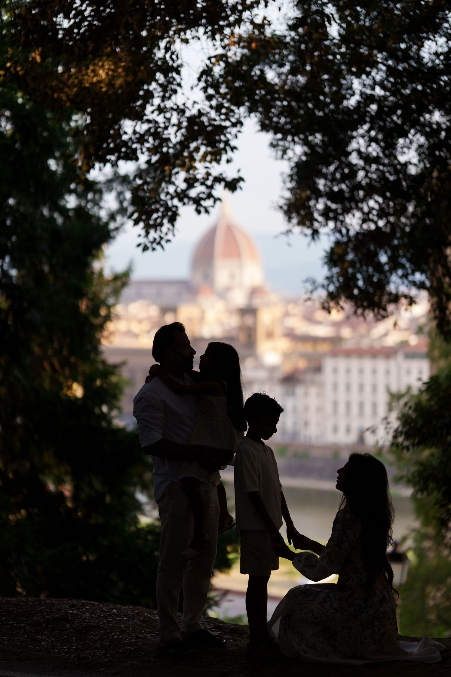Silhouette of a family with Florence Cathedral dome backdrop, framed by trees at dusk in Italy.