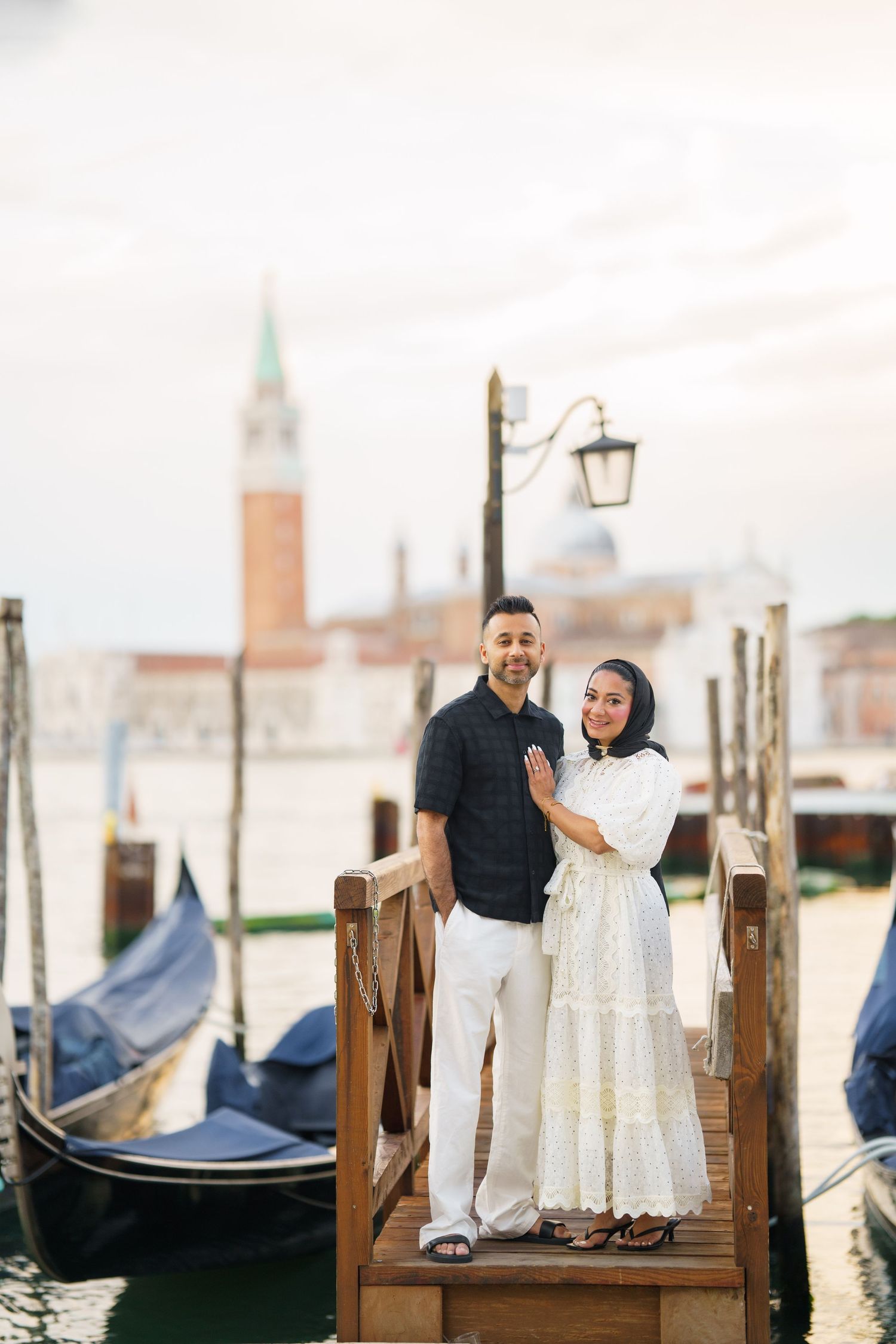 Couple posing on a wooden dock in Venice, Italy, with gondolas and San Giorgio Maggiore in the background.