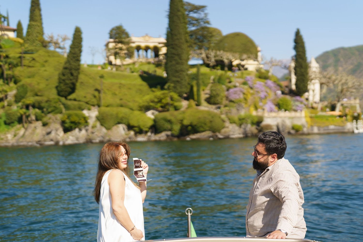 Couple on a boat at Lake Como, Italy, with lush greenery and a historic villa in the background.