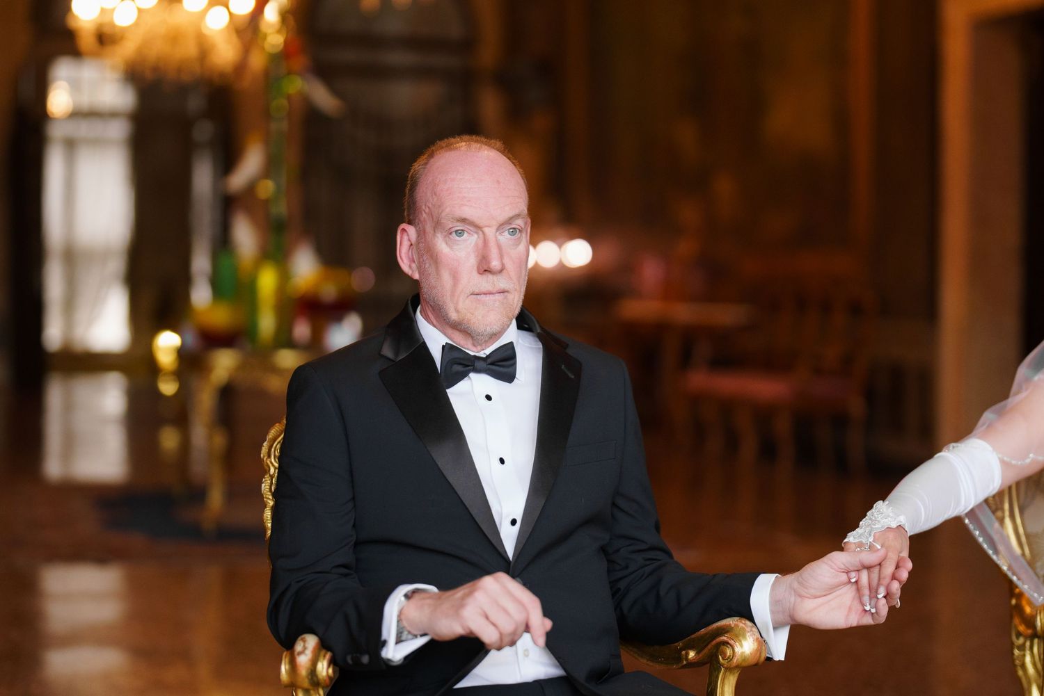 A person in a black tuxedo sits at an elegant dining table during an evening event.