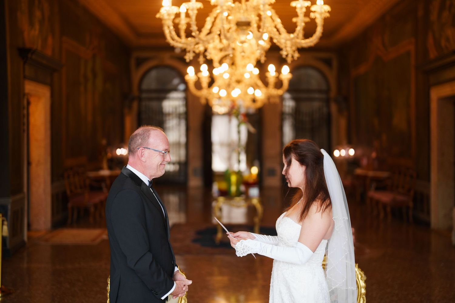 A couple shares a romantic moment under an elegant crystal chandelier during their wedding reception.