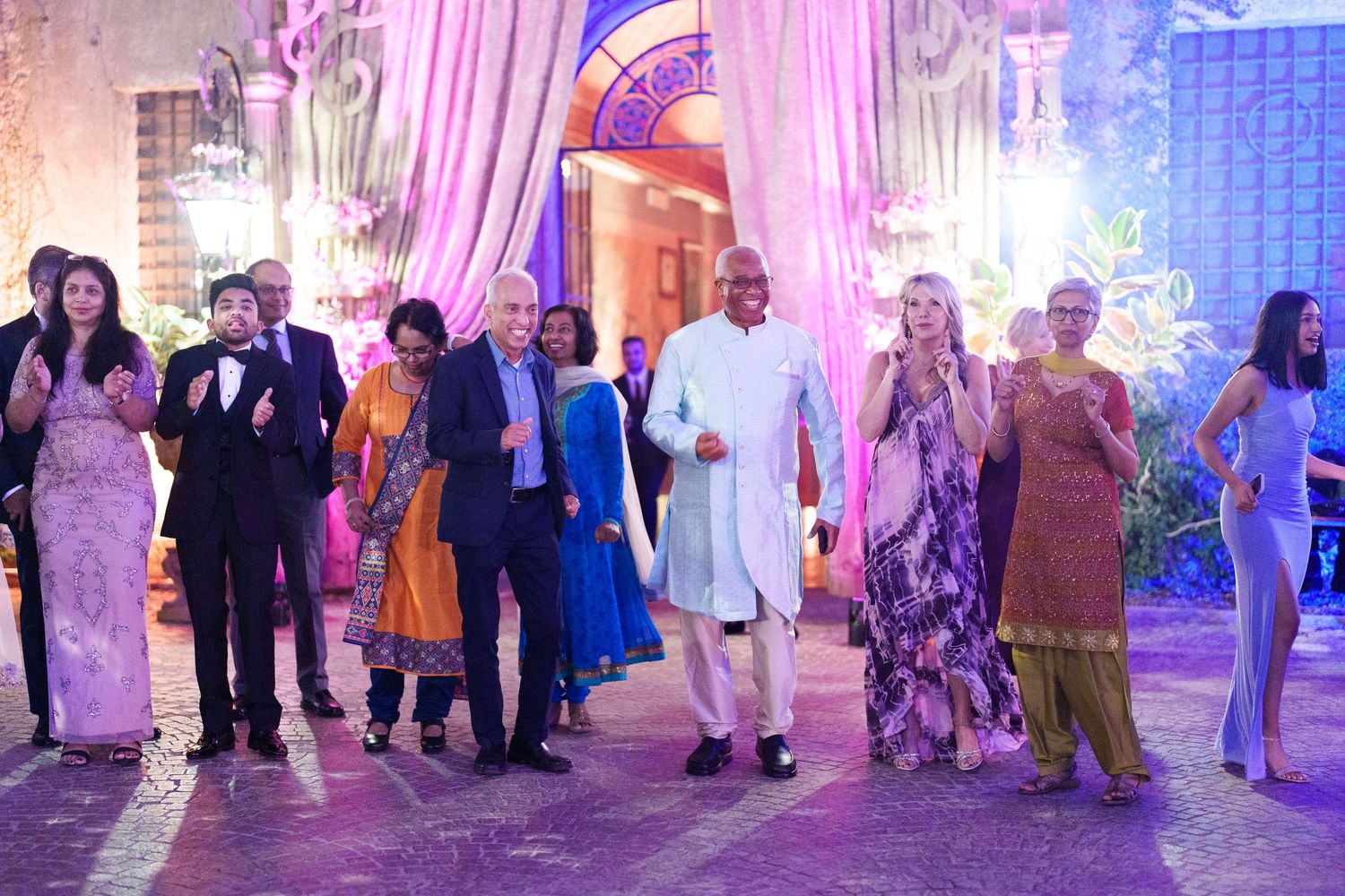 Wedding guests dancing and celebrating on a dance floor illuminated by purple and blue lighting.