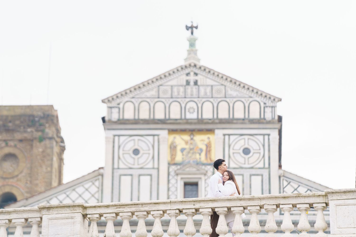 Couple posing on balcony of San Miniato al Monte church in Florence with white marble facade.