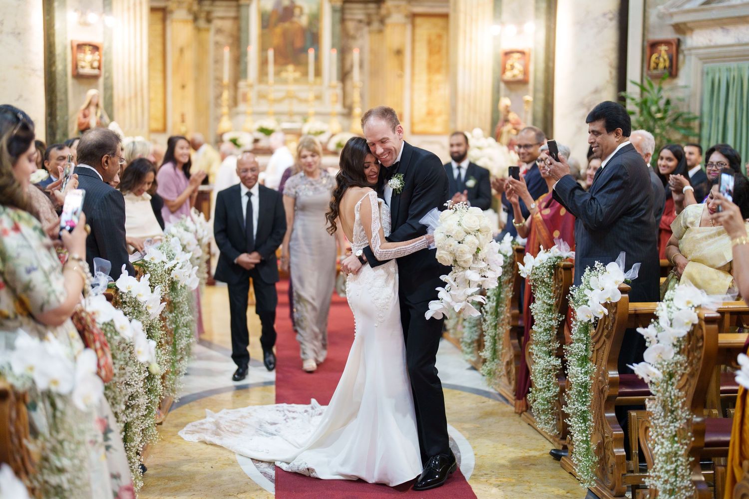 A wedding ceremony moment captured in an ornate church with floral-lined aisles.