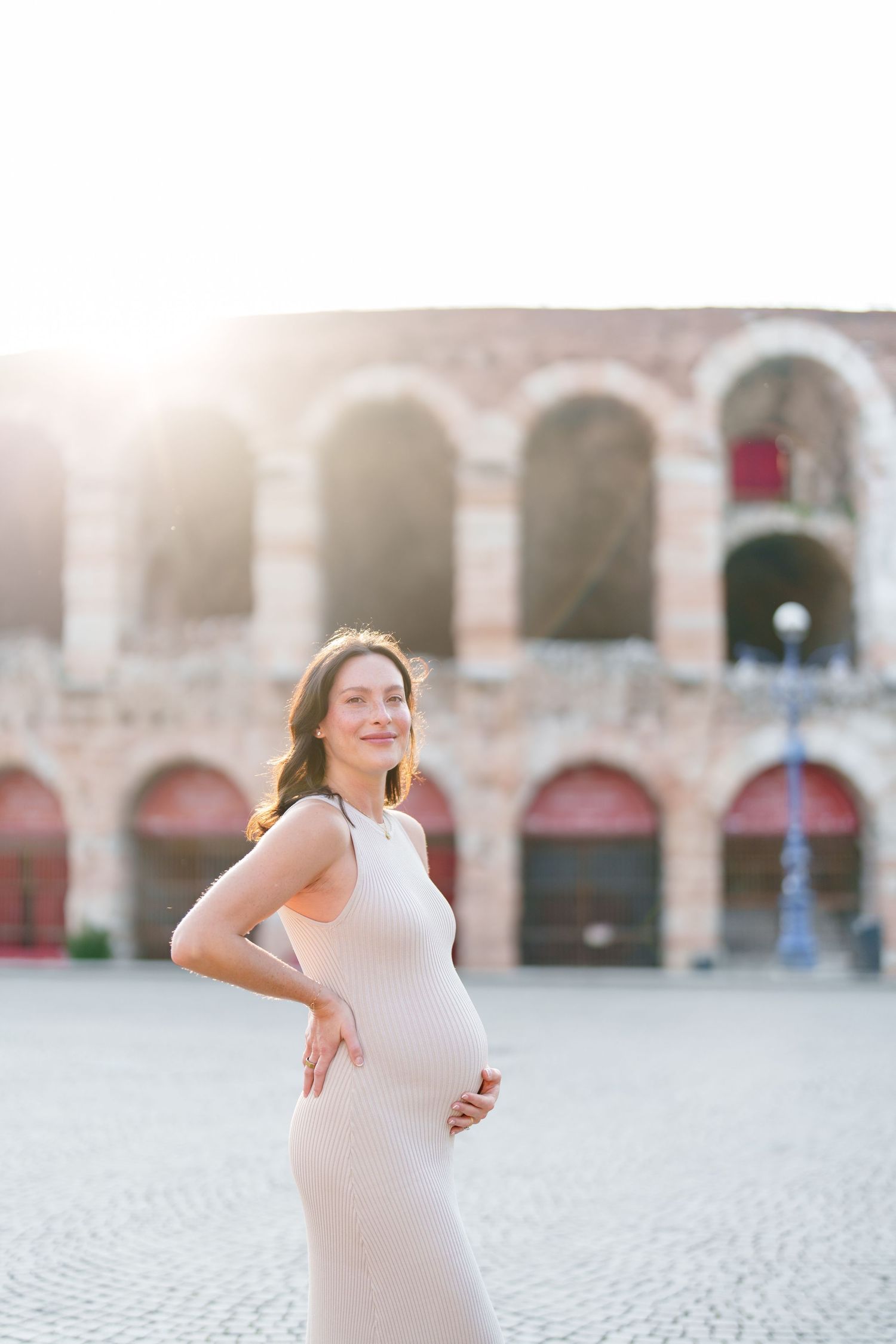 Verona photographer A person in a white dress poses joyfully in front of historic stone archways during a photo session.