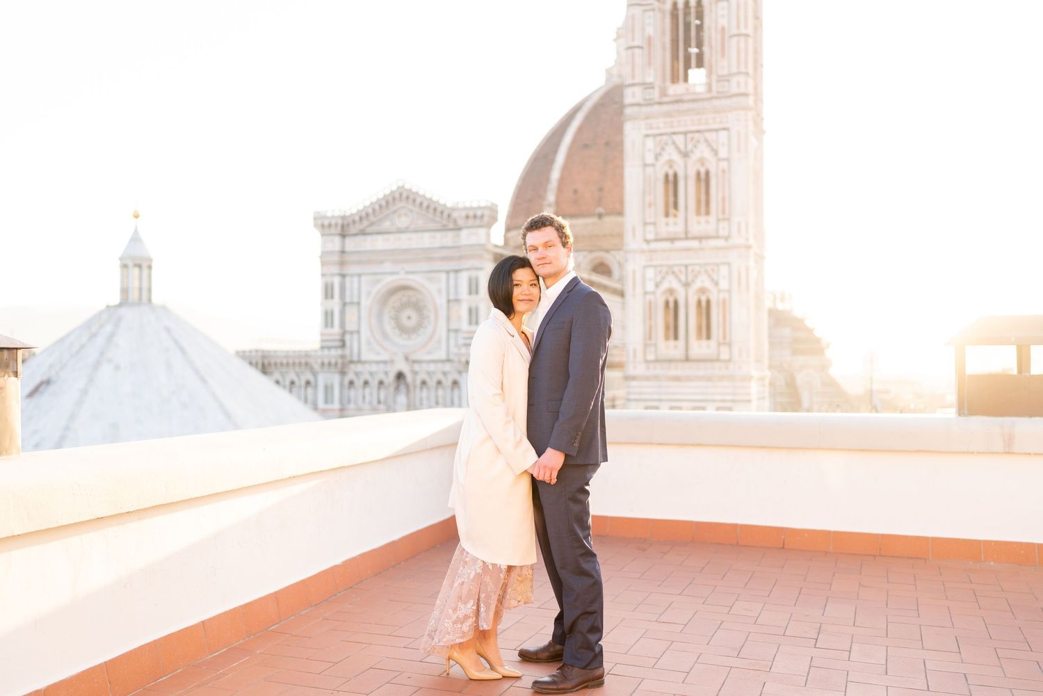 Couple poses romantically at sunset on Florence Duomo cathedral rooftop with stunning city views in background.