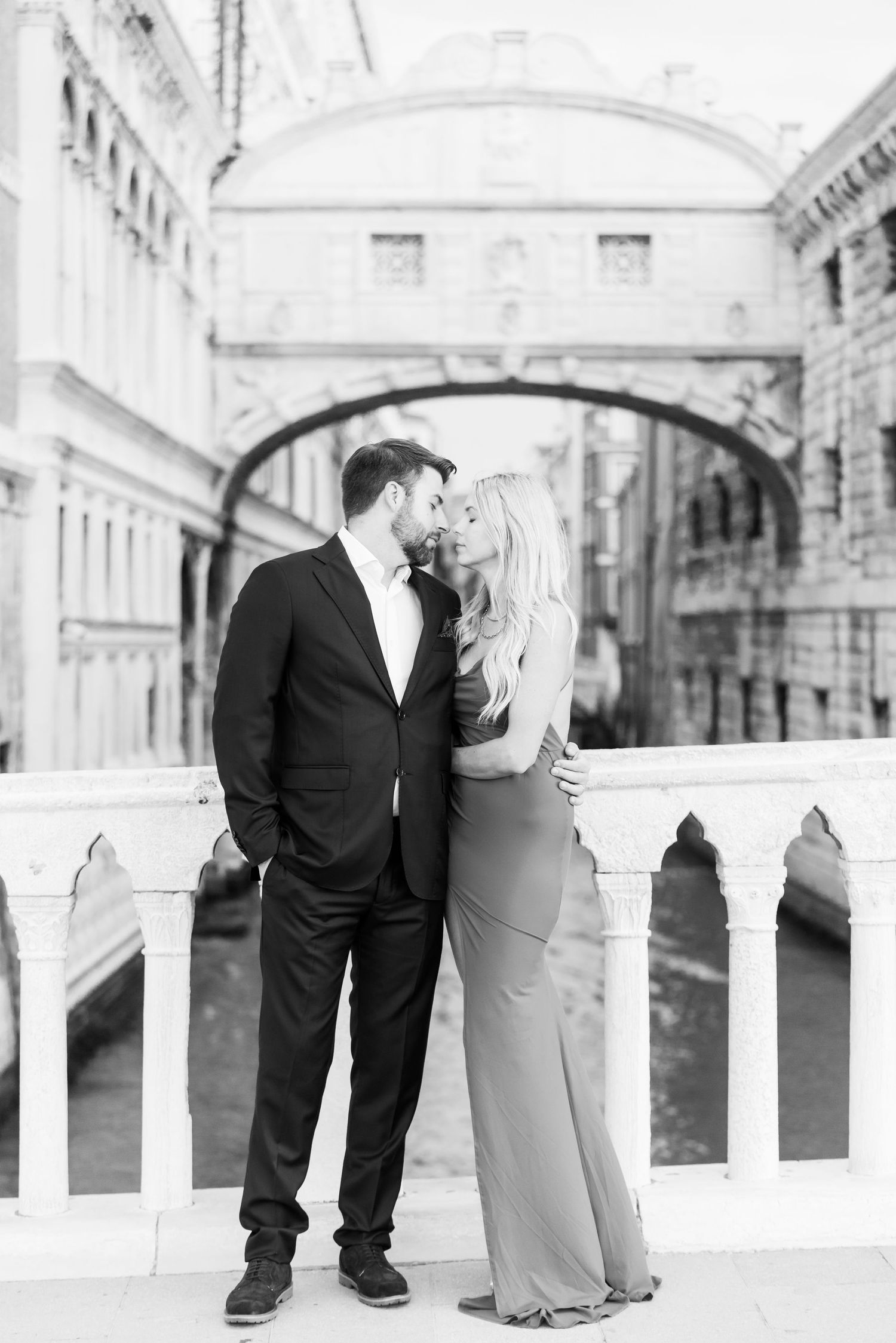 A romantic black and white photo series of a couple embracing on a classic architectural balcony with white columns.