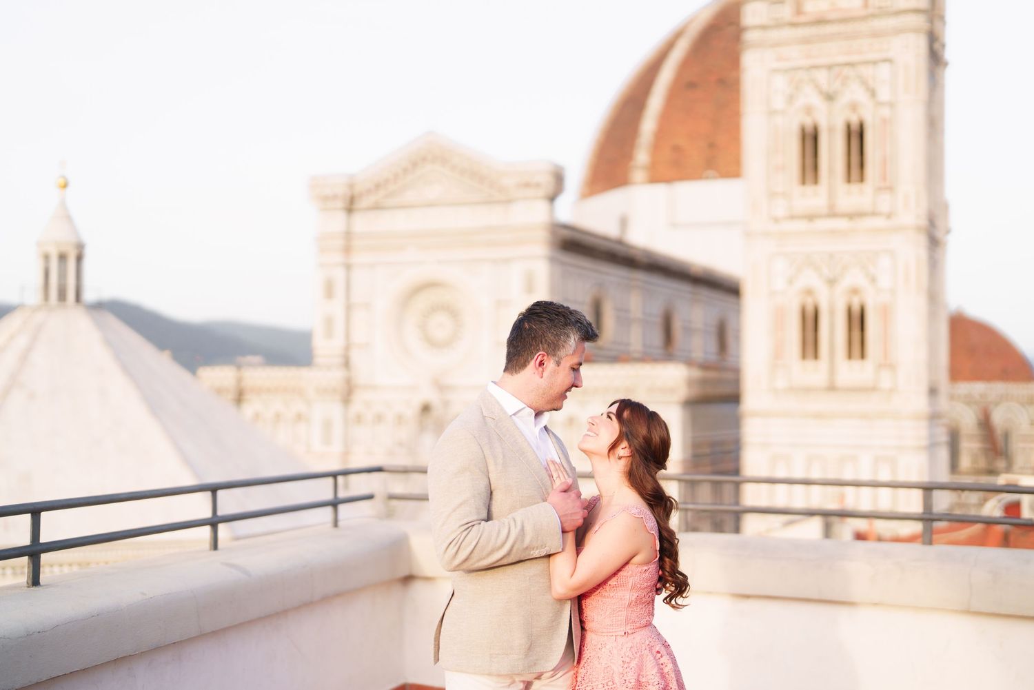 A romantic couple shares a tender moment on a rooftop terrace overlooking Florence's historic Duomo cathedral in Italy.