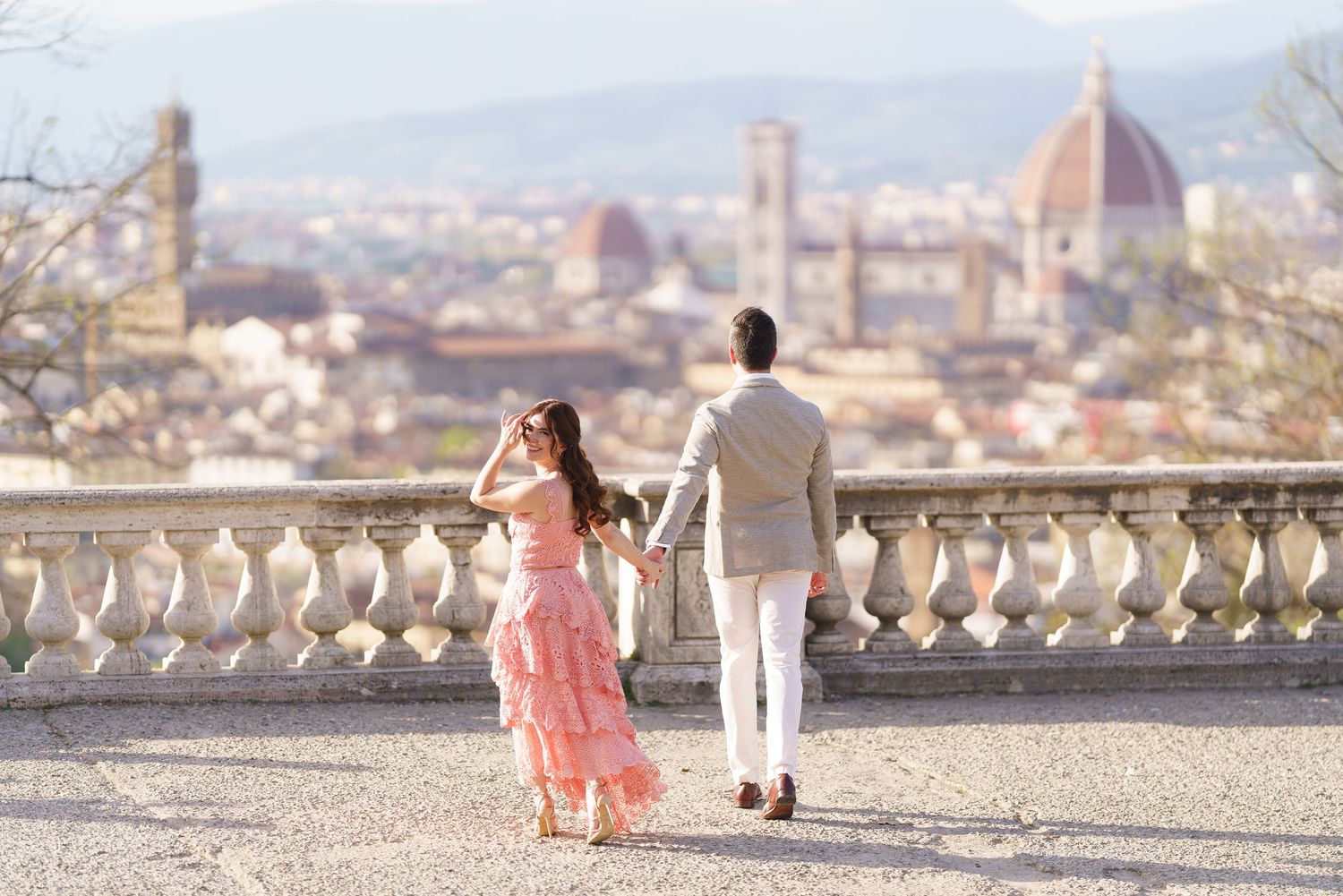 A couple stands at a scenic overlook with the iconic Florence Cathedral dome and cityscape visible in the background.