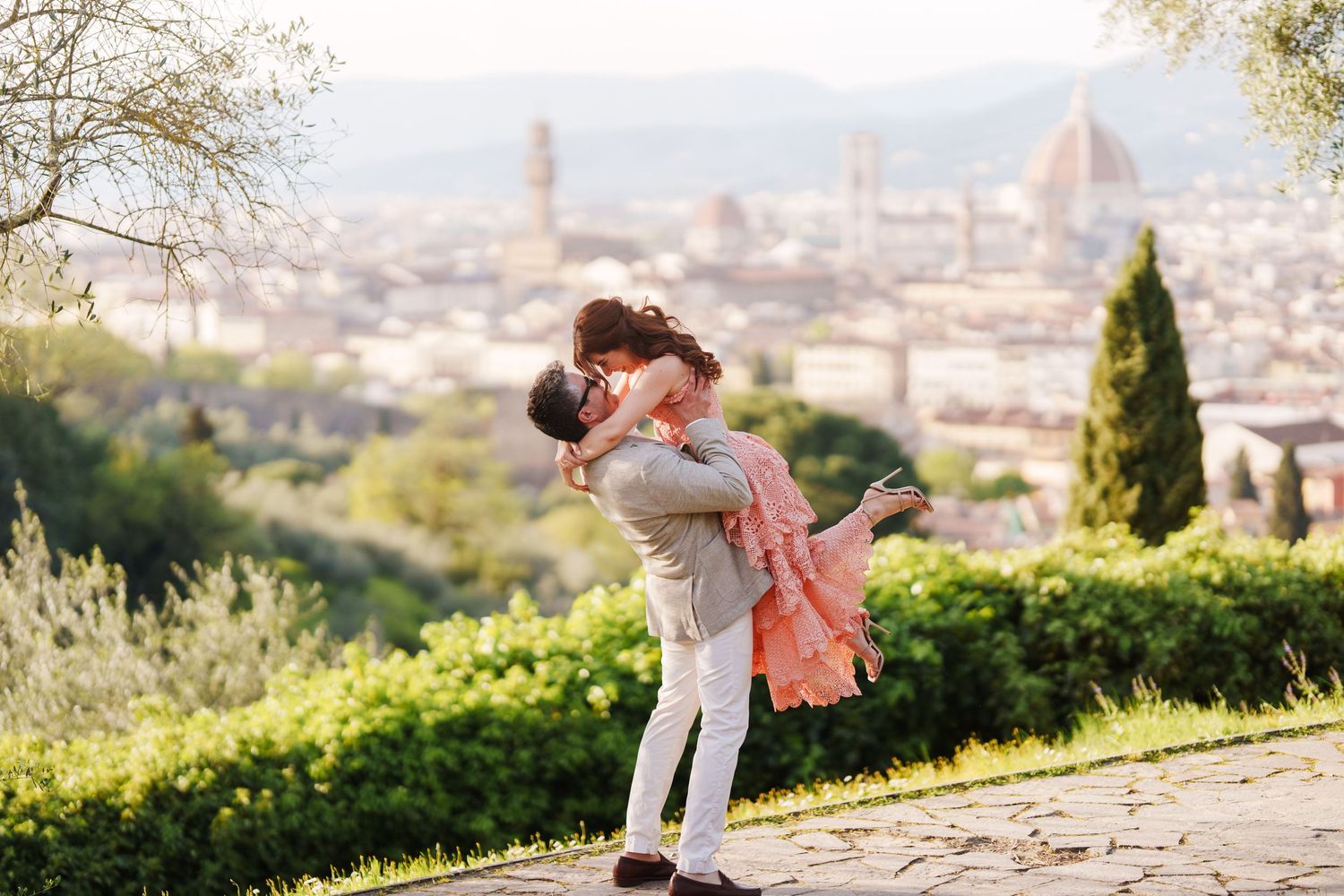 A romantic couple embraces on a hilltop overlooking the beautiful cityscape of Florence, Italy with the Duomo visible in the distance.