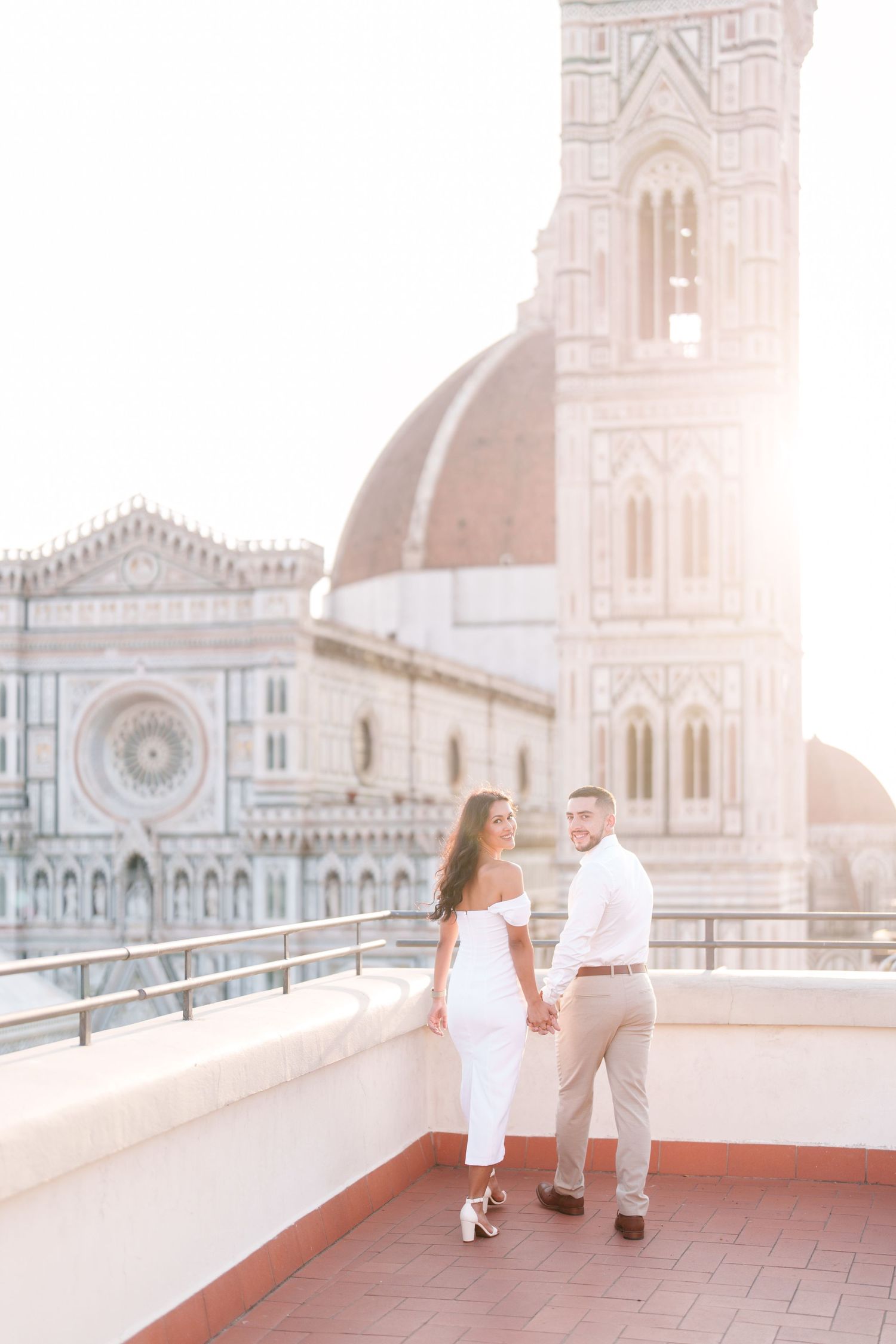 A couple enjoys a romantic moment on a rooftop terrace overlooking Florence Cathedral during golden hour in Italy.