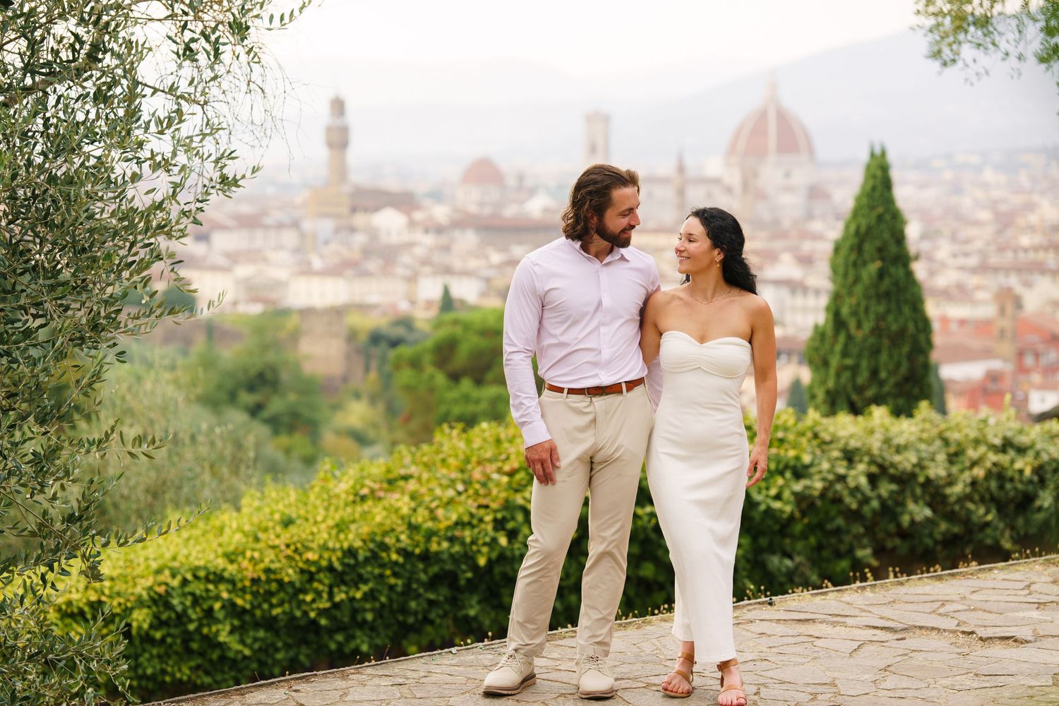A couple shares a romantic moment overlooking the historic skyline of Florence, Italy from a scenic hilltop viewpoint.