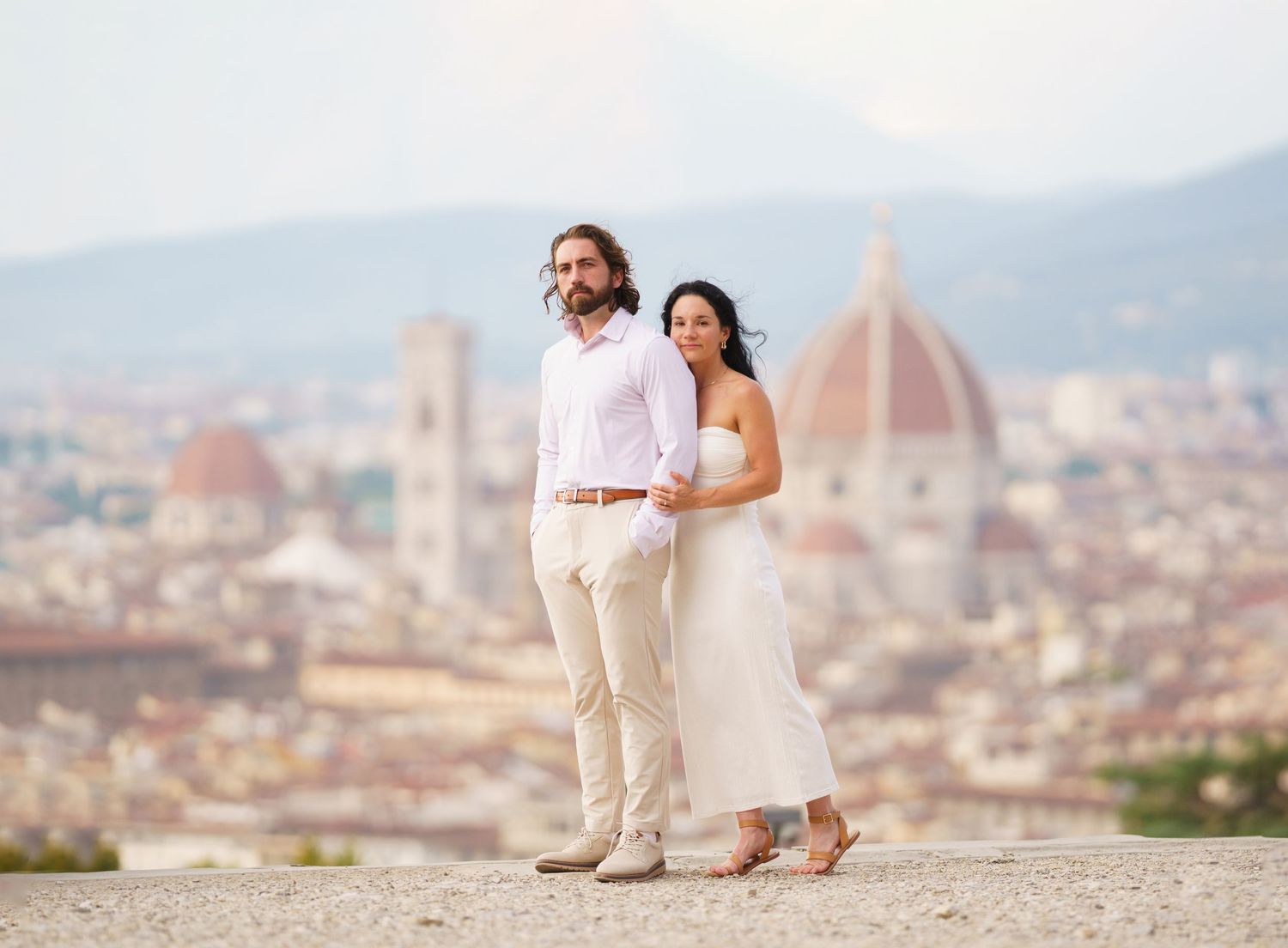 Romantic couple in white outfits admiring Florence cityscape from Piazzale Michelangelo viewpoint.