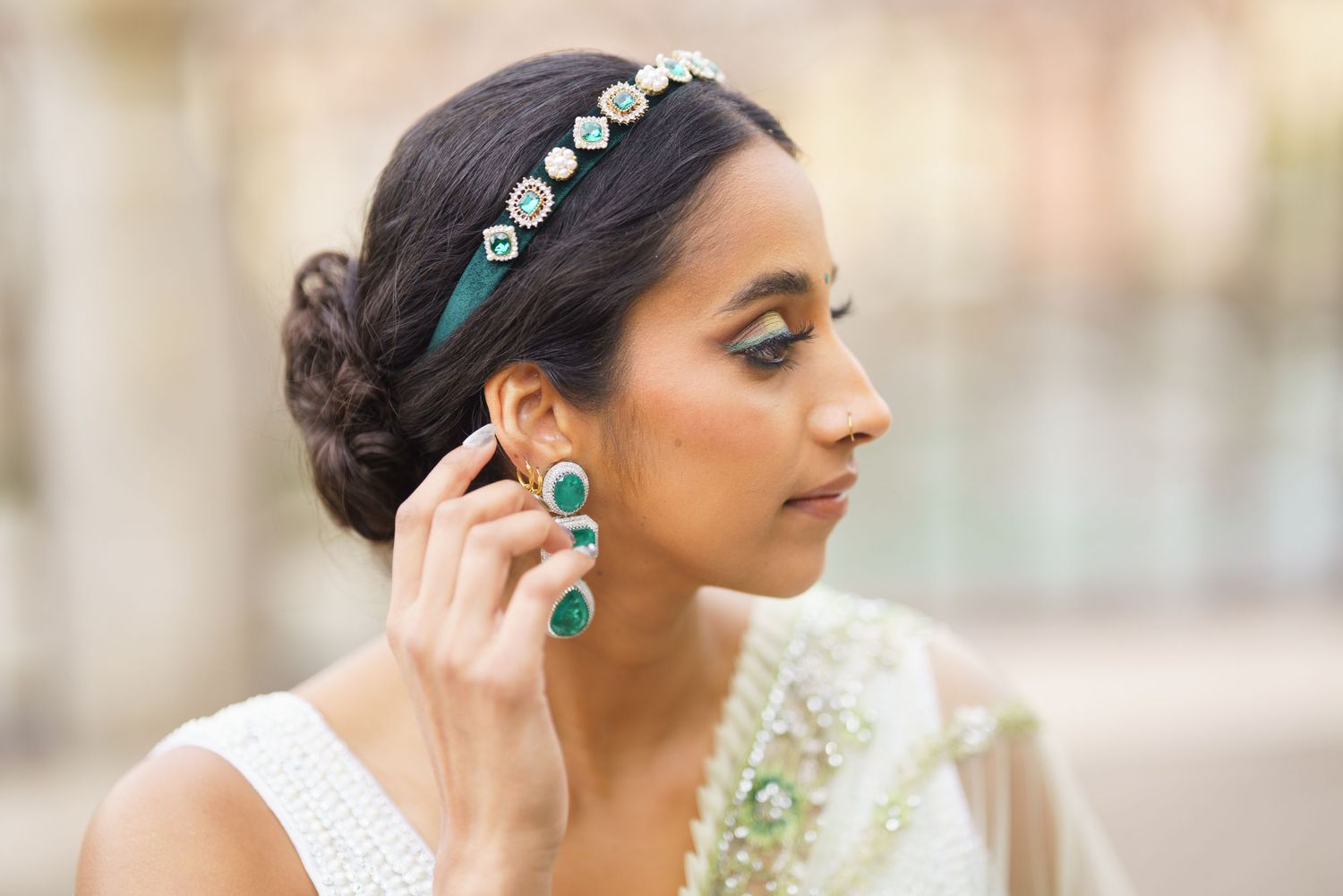 A bride wearing a crystal headpiece and elegant updo hairstyle poses in profile against a soft blurred background.