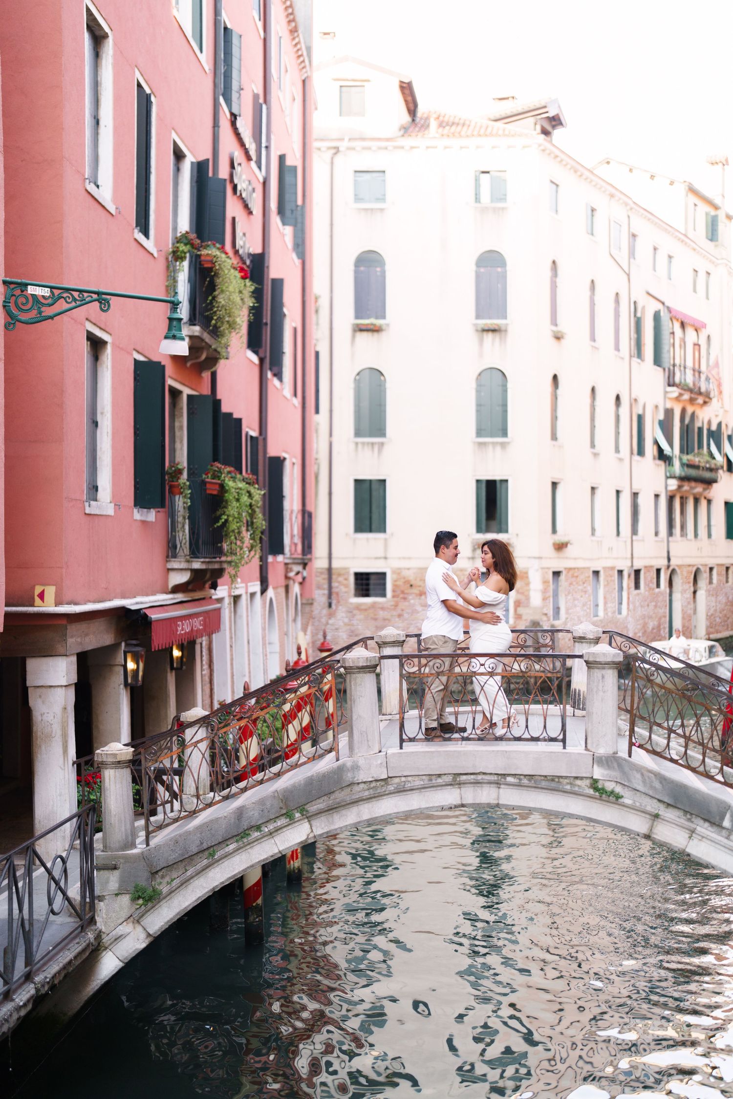 Pink and white buildings line a narrow Venetian canal with arched bridges and reflective water in Venice, Italy.