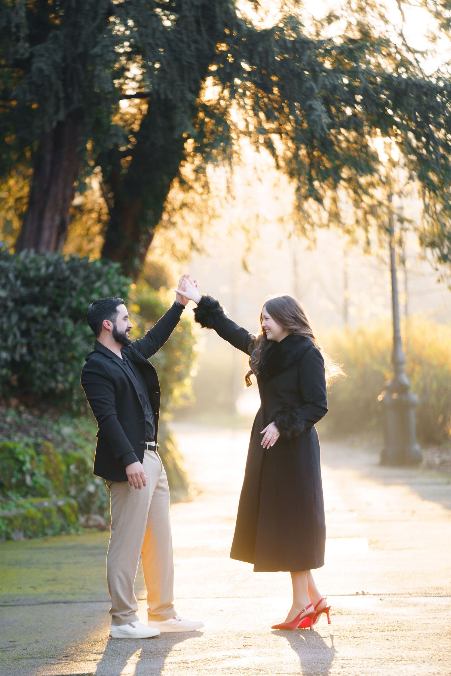 Two people share a romantic moment in a park at sunset with sunlight streaming through trees.