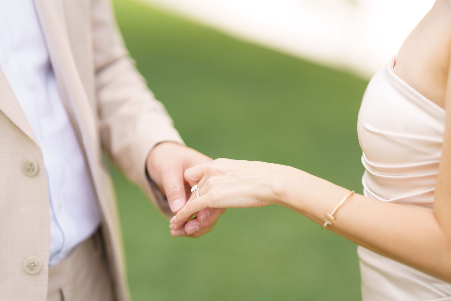 Close-up shot of hands exchanging wedding rings during an outdoor ceremony against a green background.