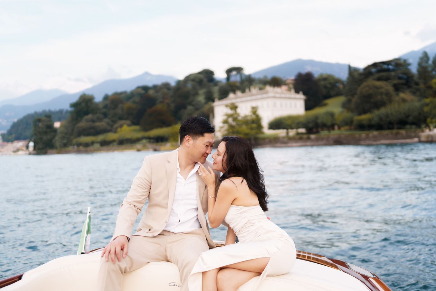 A couple shares romantic moments together in a boat on a scenic lake with mountains in the background.