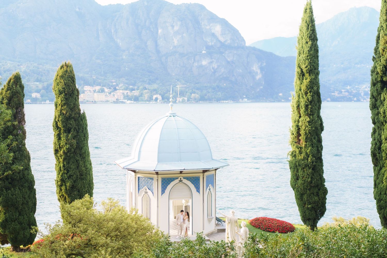 Scenic Lake Como waterfront view with cypress trees and mountains in Bellagio, Italy.