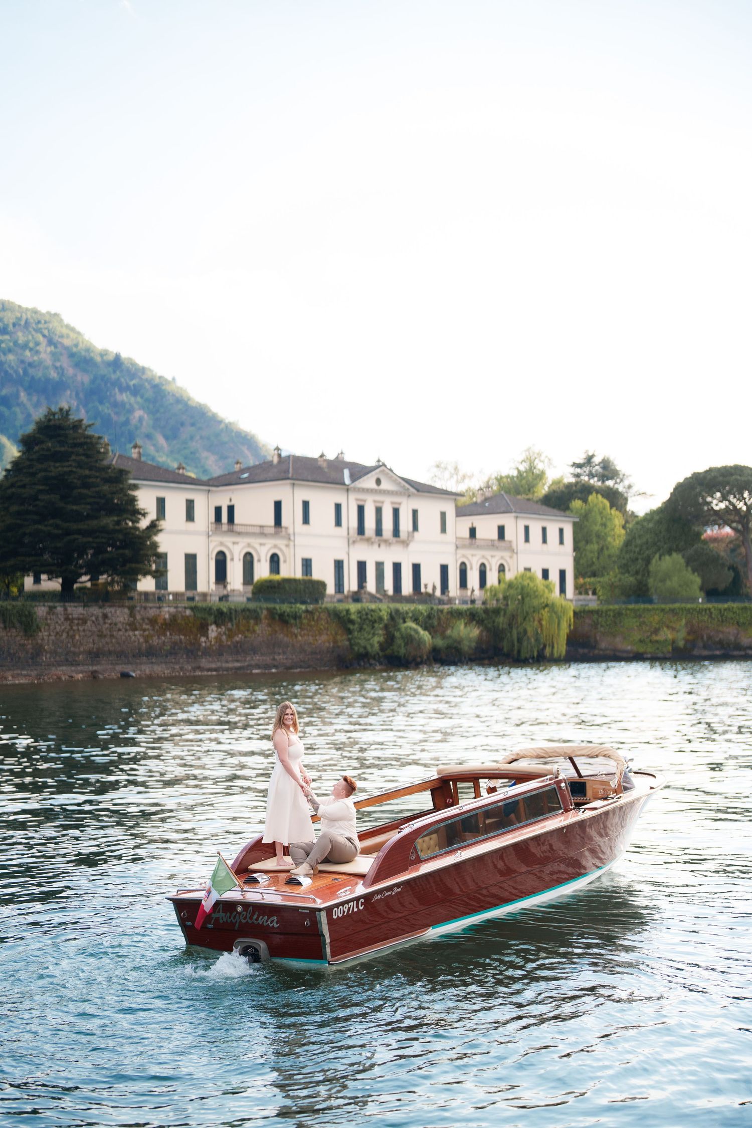 Couple in wedding attire riding a classic wooden boat on Lake Como with an elegant Italian villa in the background.