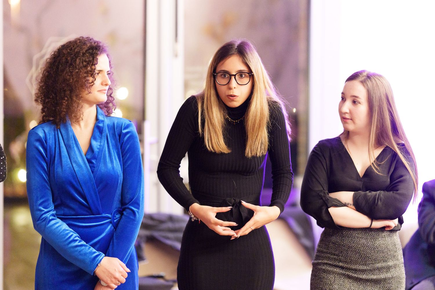 Three professional women in elegant attire engaged in conversation at a formal indoor event.