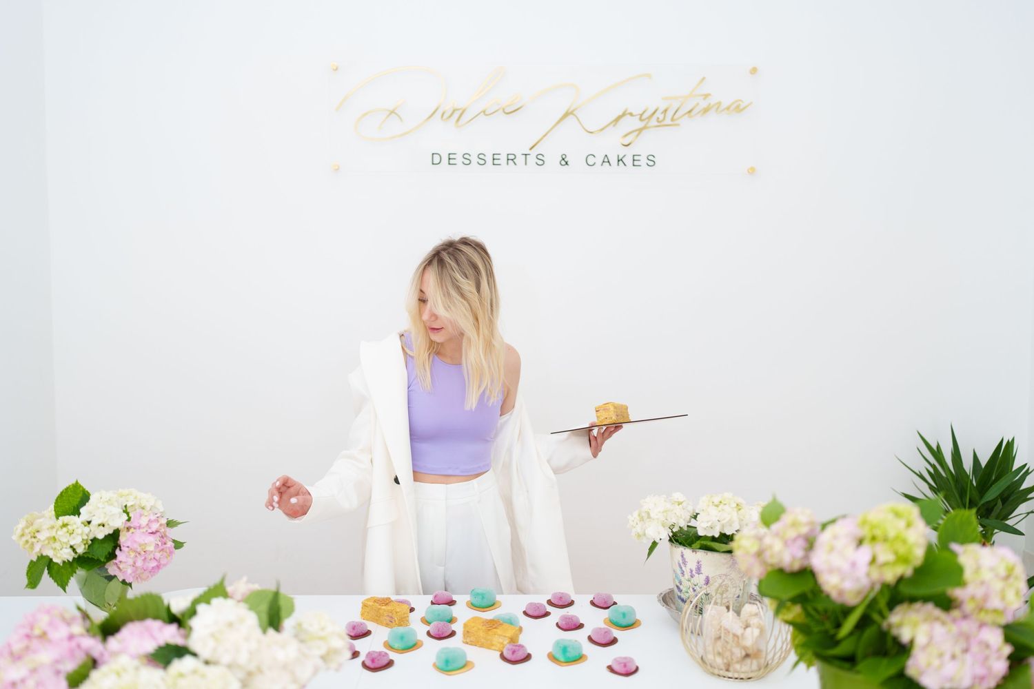 Woman arranging colorful macarons at a dessert table with flowers at Miss Krystina Desserts and Cakes shop.