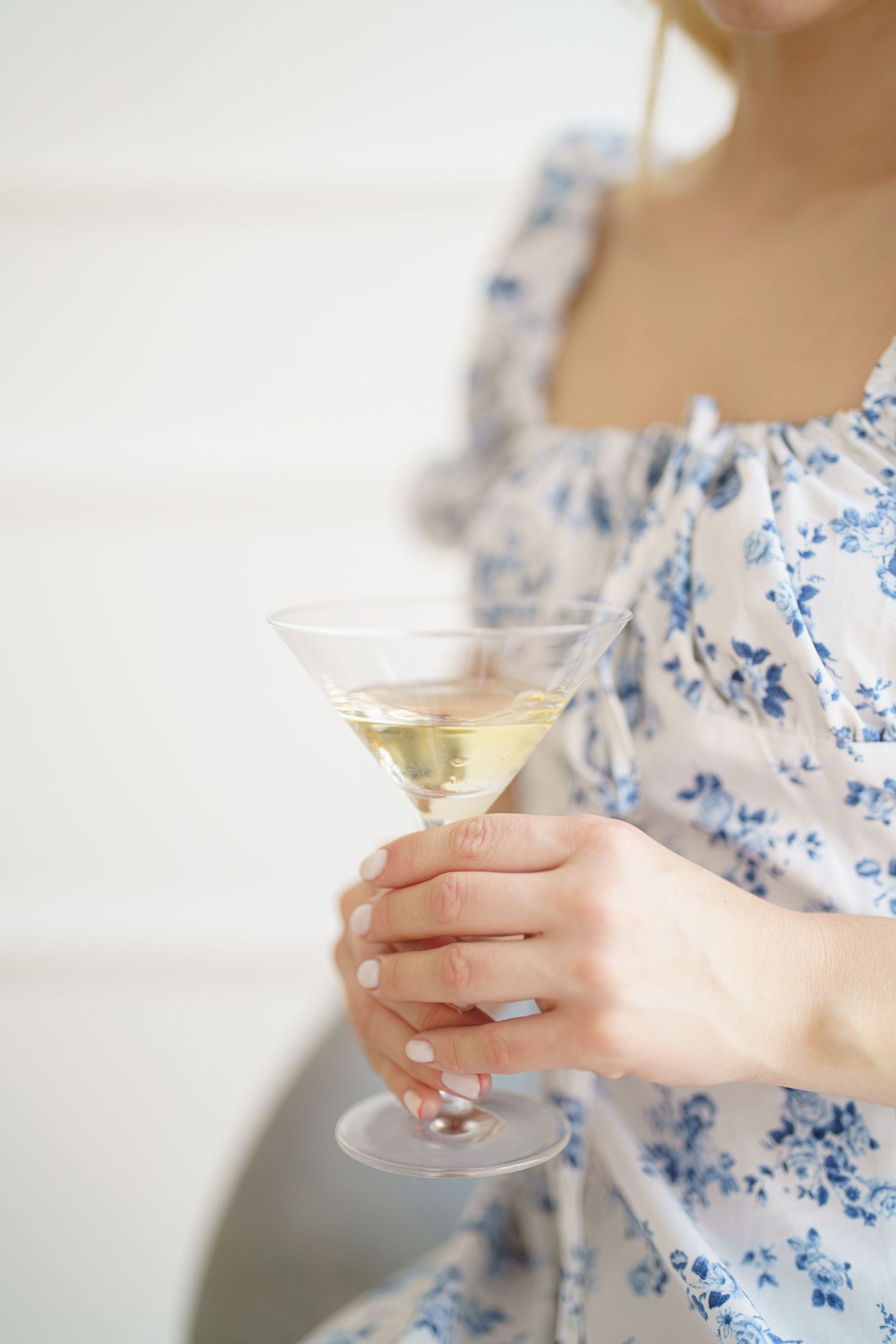 Woman in blue floral dress holding a martini glass with a light yellow cocktail and olive garnish.