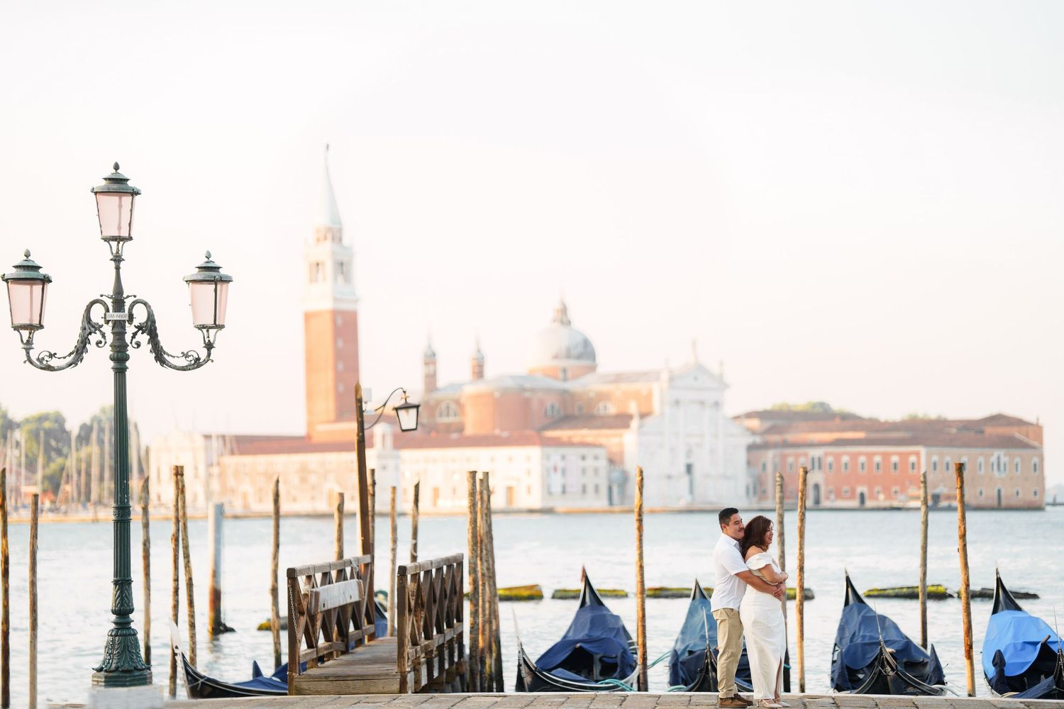 photographer venice Panoramic view of Venice waterfront with ornate lampposts and gondolas along misty canal at dawn.