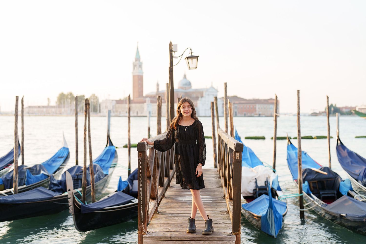 Traditional Venetian gondolas moored along wooden posts in the Grand Canal with historic buildings in the background.