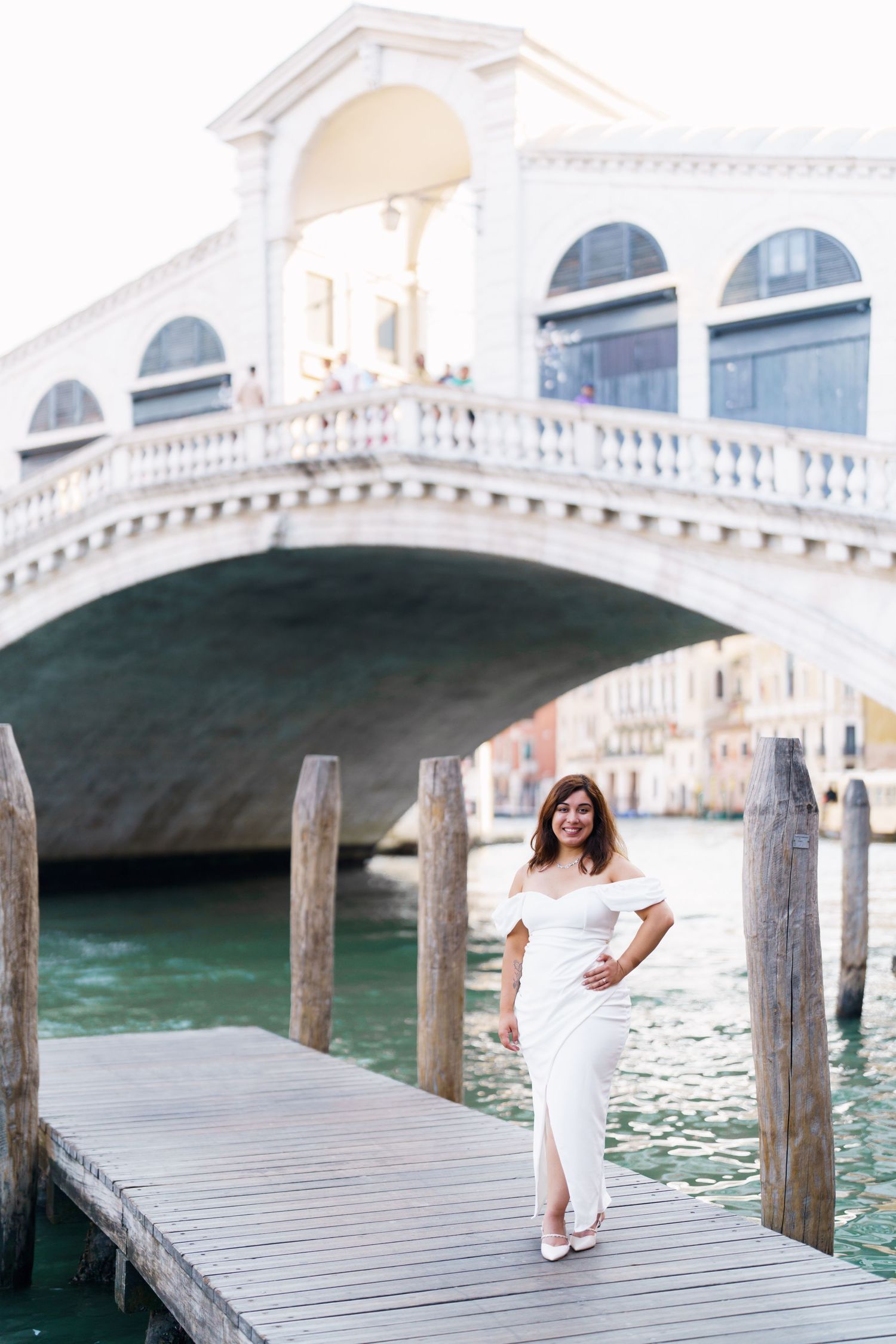 photographer venice A romantic scene on a wooden dock in Venice with turquoise water and white stone bridges in the background.