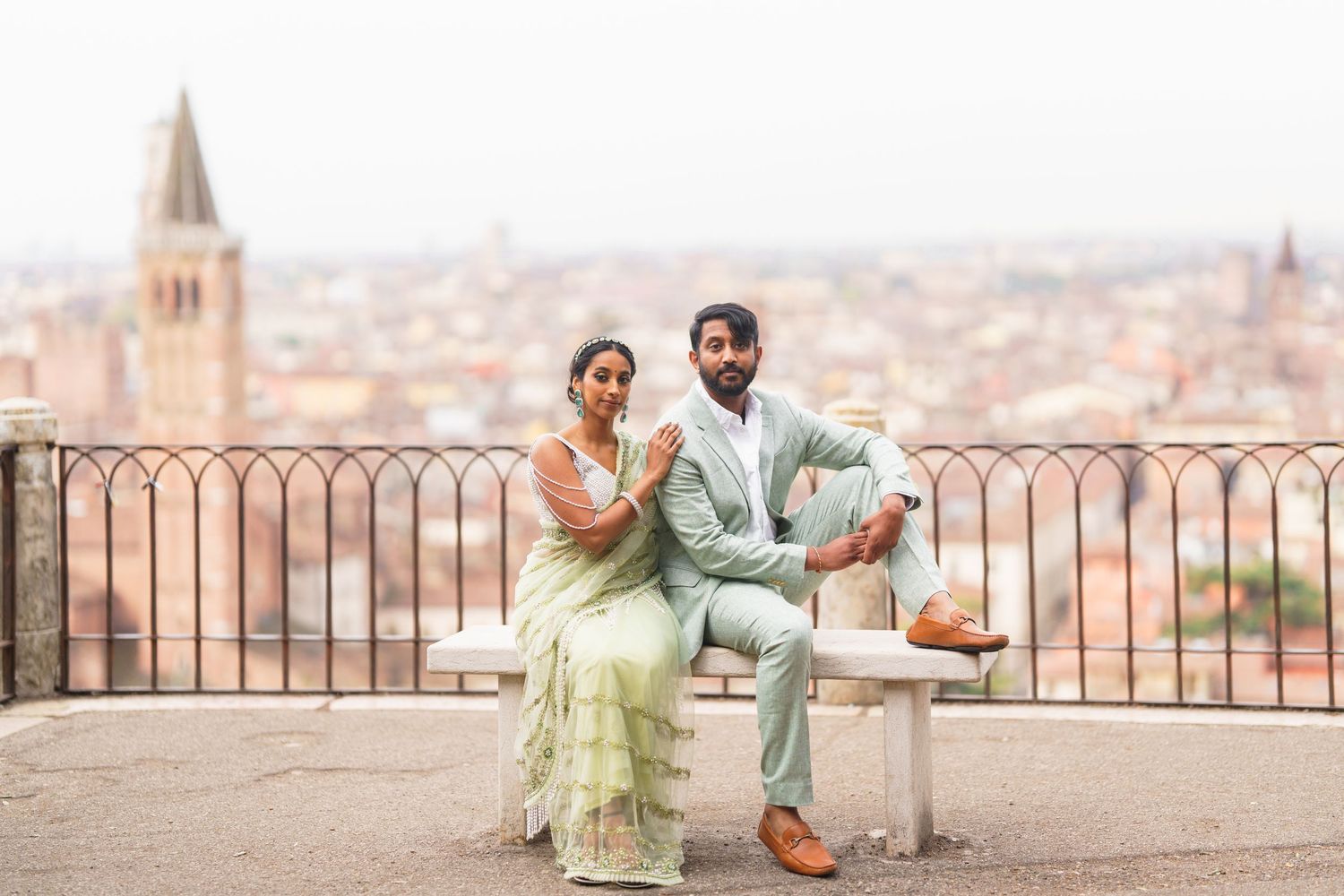 A couple poses together on a scenic overlook terrace with a panoramic view of Bologna, Italy in the background.