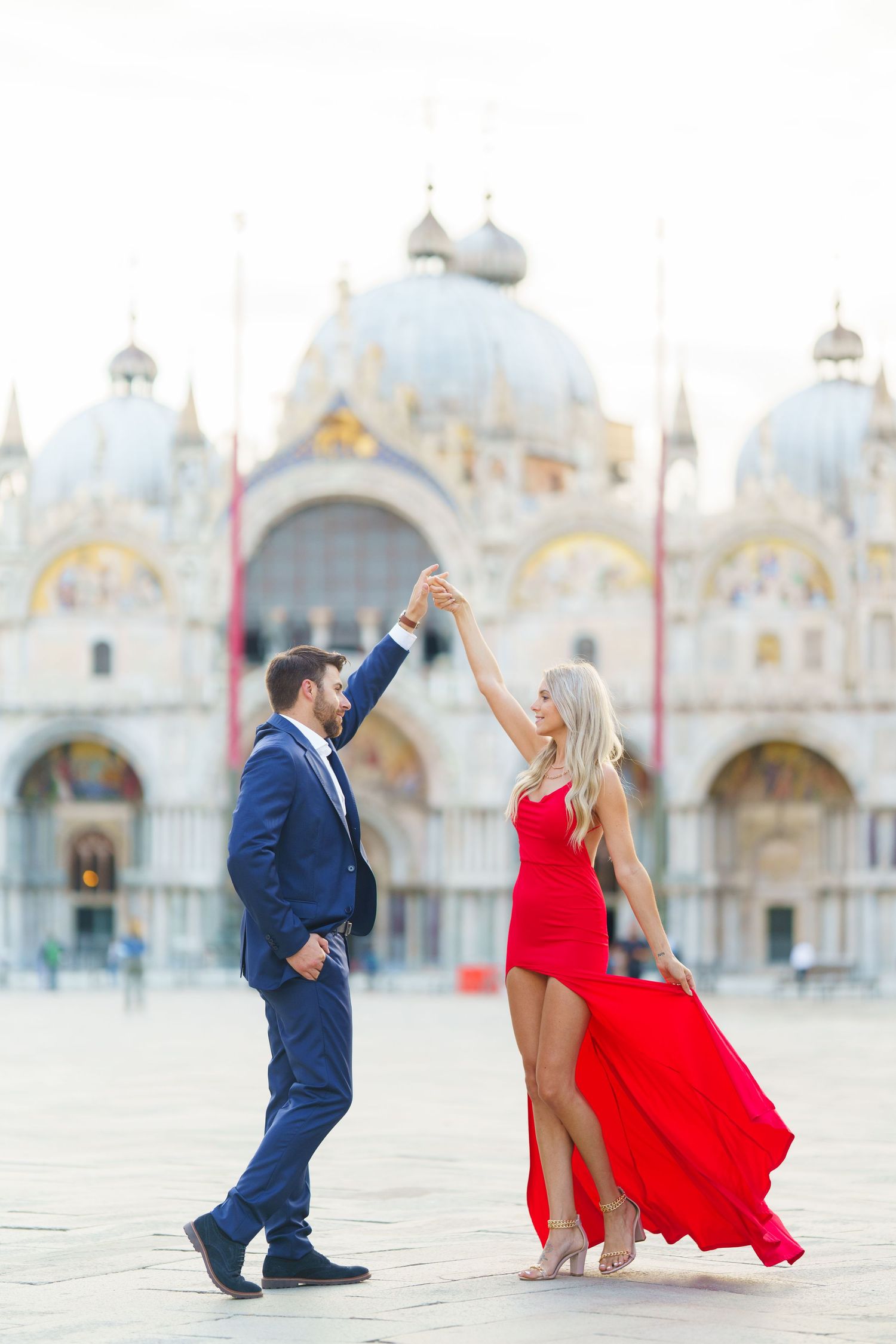 Couple dancing in front of St. Mark's Basilica in Venice, with woman wearing flowing red dress and man in navy suit.