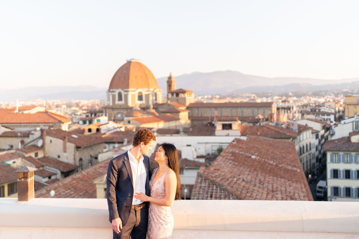 A couple embraces while enjoying the sunset view over Florence, Italy's iconic terracotta rooftops and Duomo cathedral.