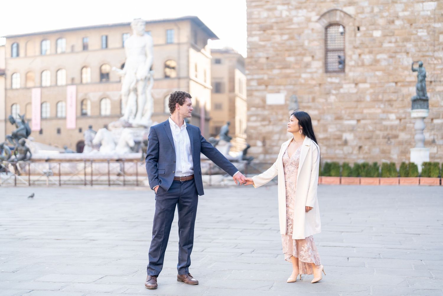 A couple in formal attire poses for photos in front of an elegant stone building exterior.