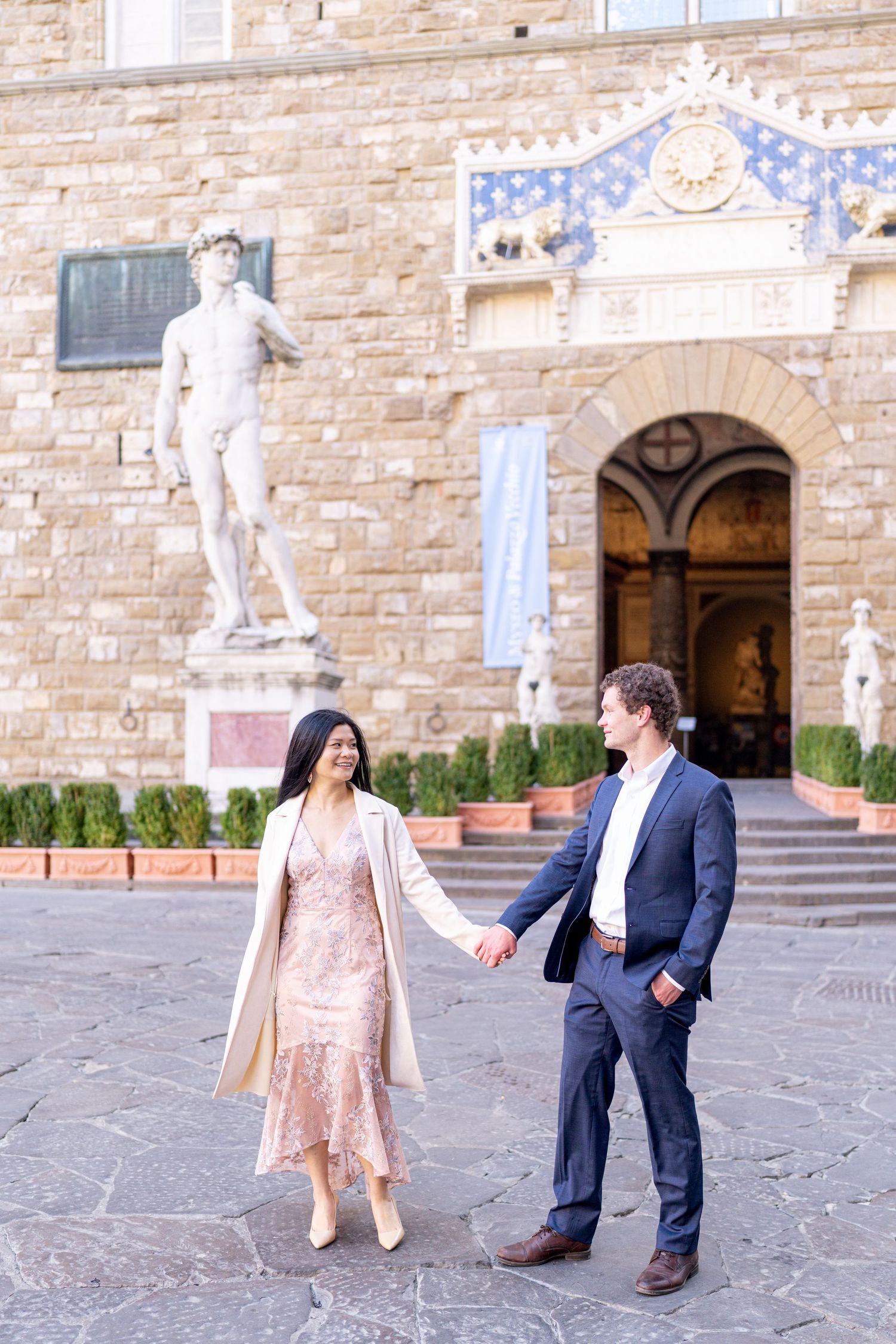 Romantic couple dancing and twirling together in front of historic stone building facade with statues.
