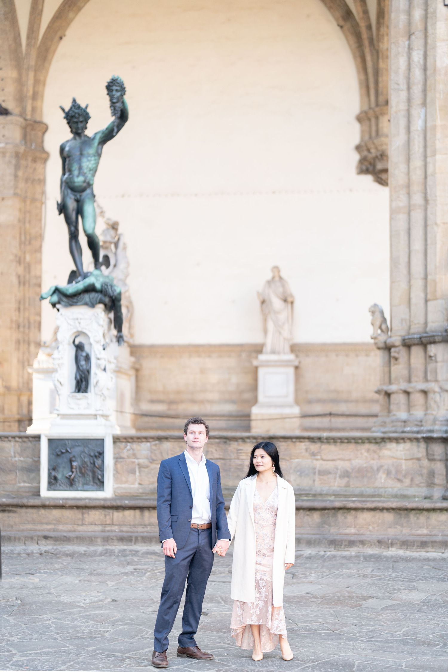 A couple stands beneath an arched gallery with historic statues and sculptures in Florence, Italy.