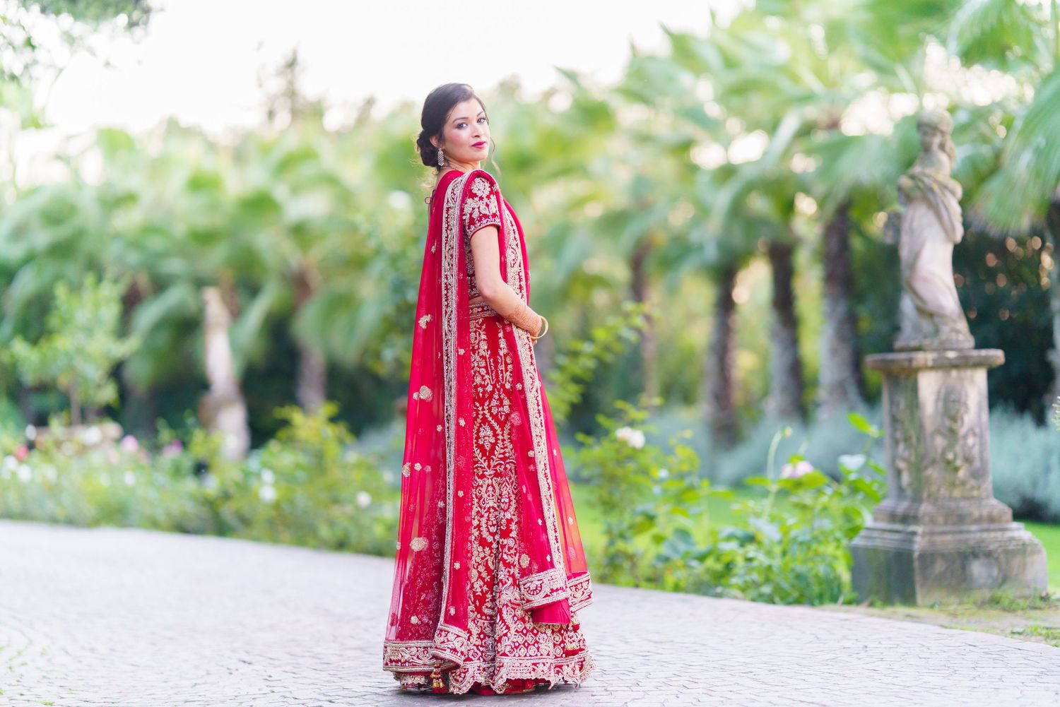 Traditional red bridal lehenga captured in an outdoor garden setting.