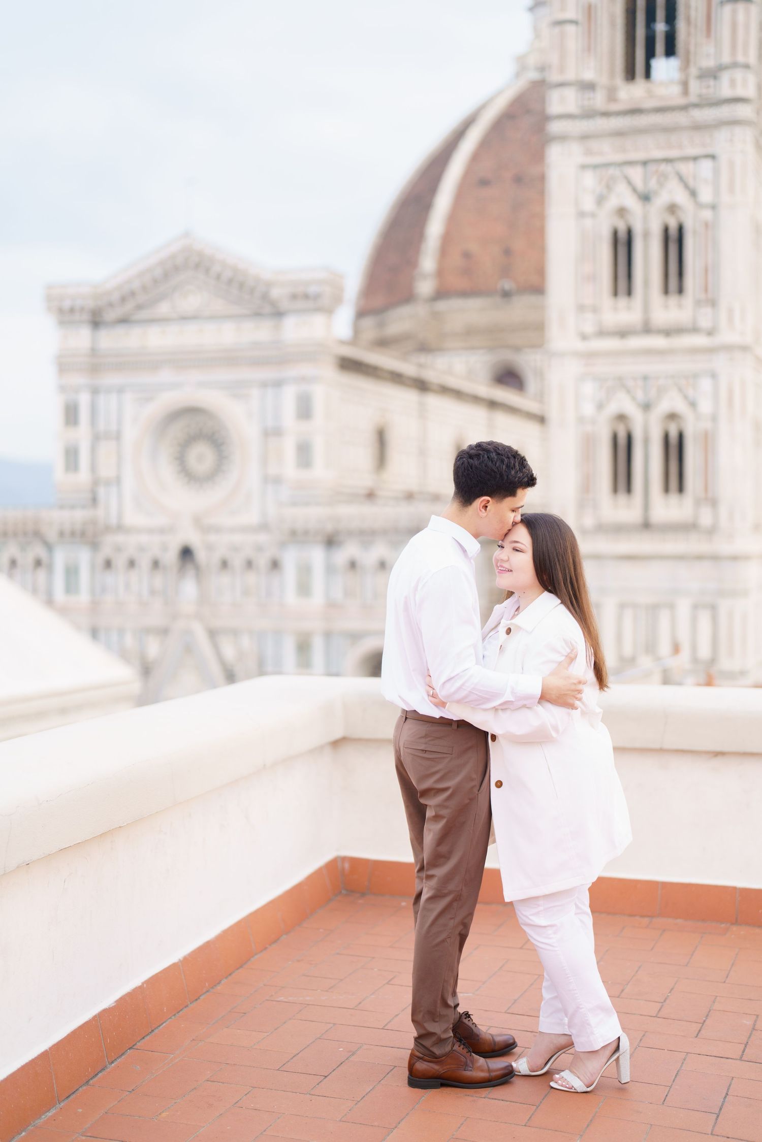 Couple in coordinated outfits posing on terrace with Duomo di Firenze backdrop.