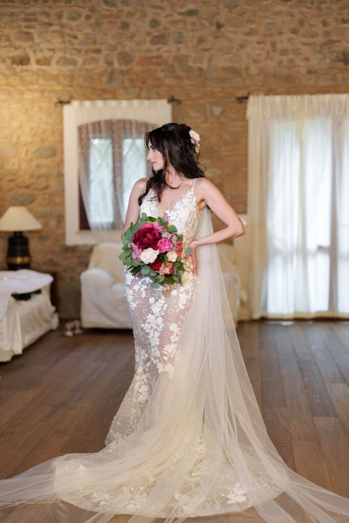 Bride in lace wedding gown with flowing cathedral veil posing in rustic stone room.