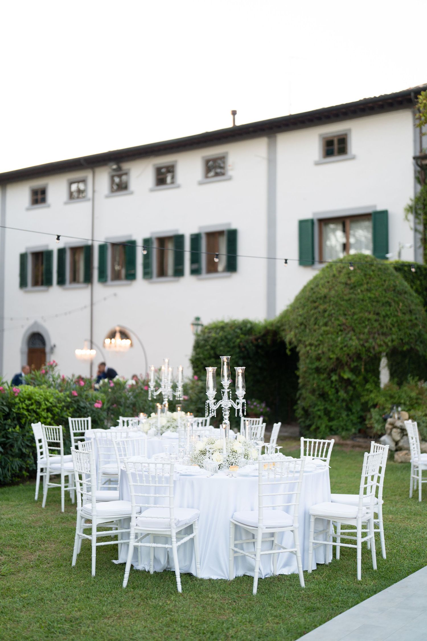 White wedding reception tables and chairs arranged on lawn in front of Italian villa.