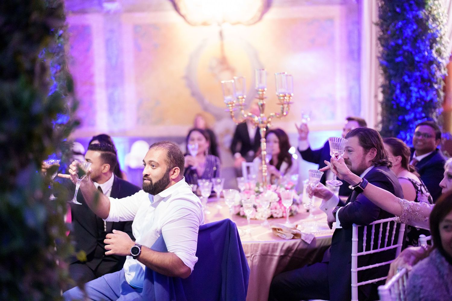 Wedding reception tables set with elegant centerpieces under dramatic purple and blue lighting.