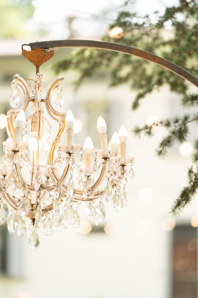 Elegant crystal chandelier with white candle lights hanging against a soft white background.