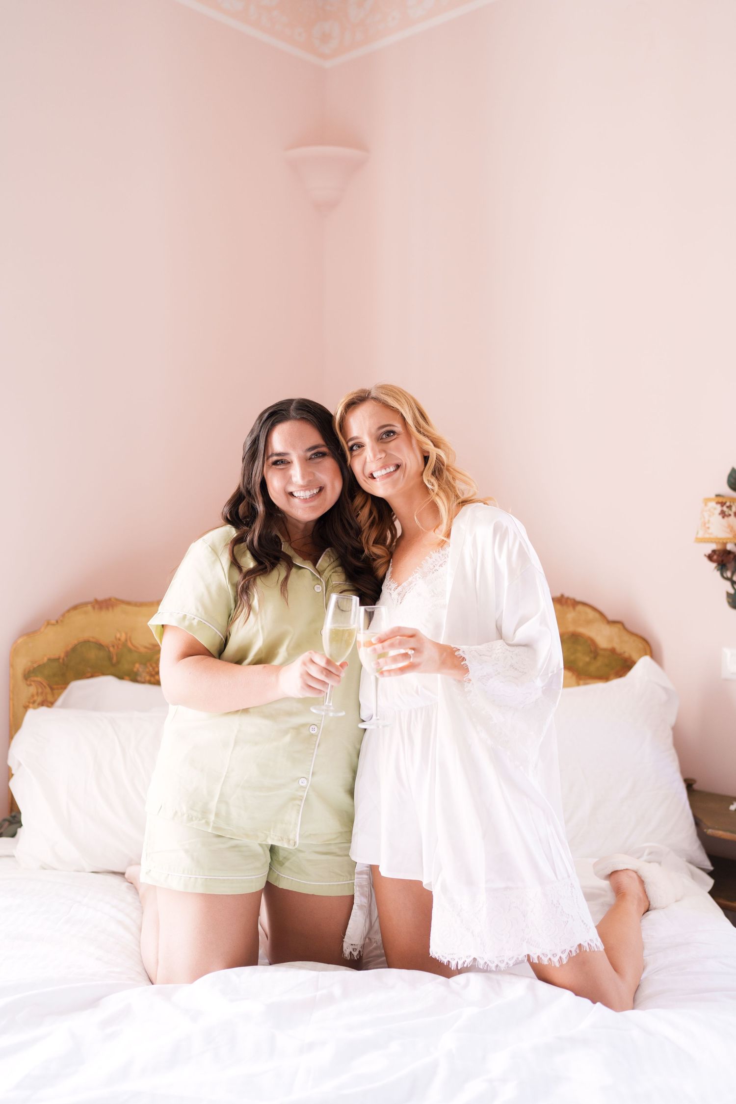 Friends sharing laughs while sitting together on a bed with decorative headboard.