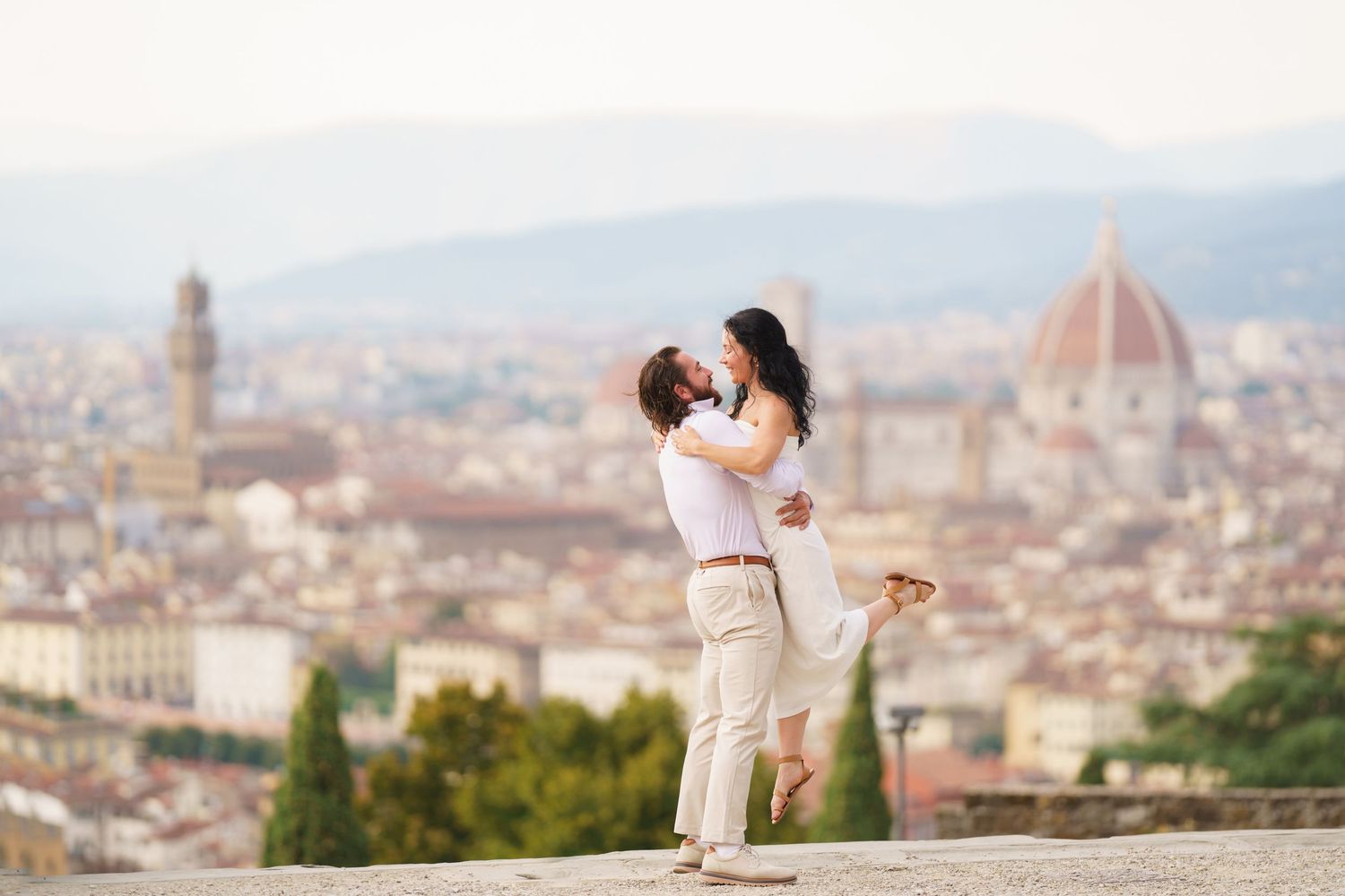 A romantic couple embraces while overlooking the stunning cityscape of Florence, Italy with its iconic Duomo cathedral.