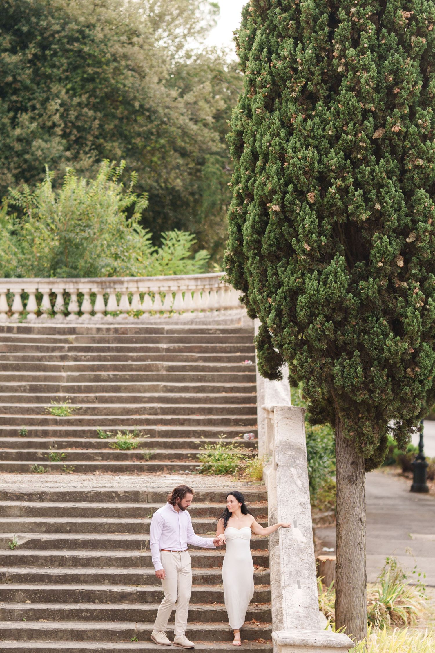 A couple shares a romantic moment on stone steps surrounded by lush greenery in an outdoor garden setting.