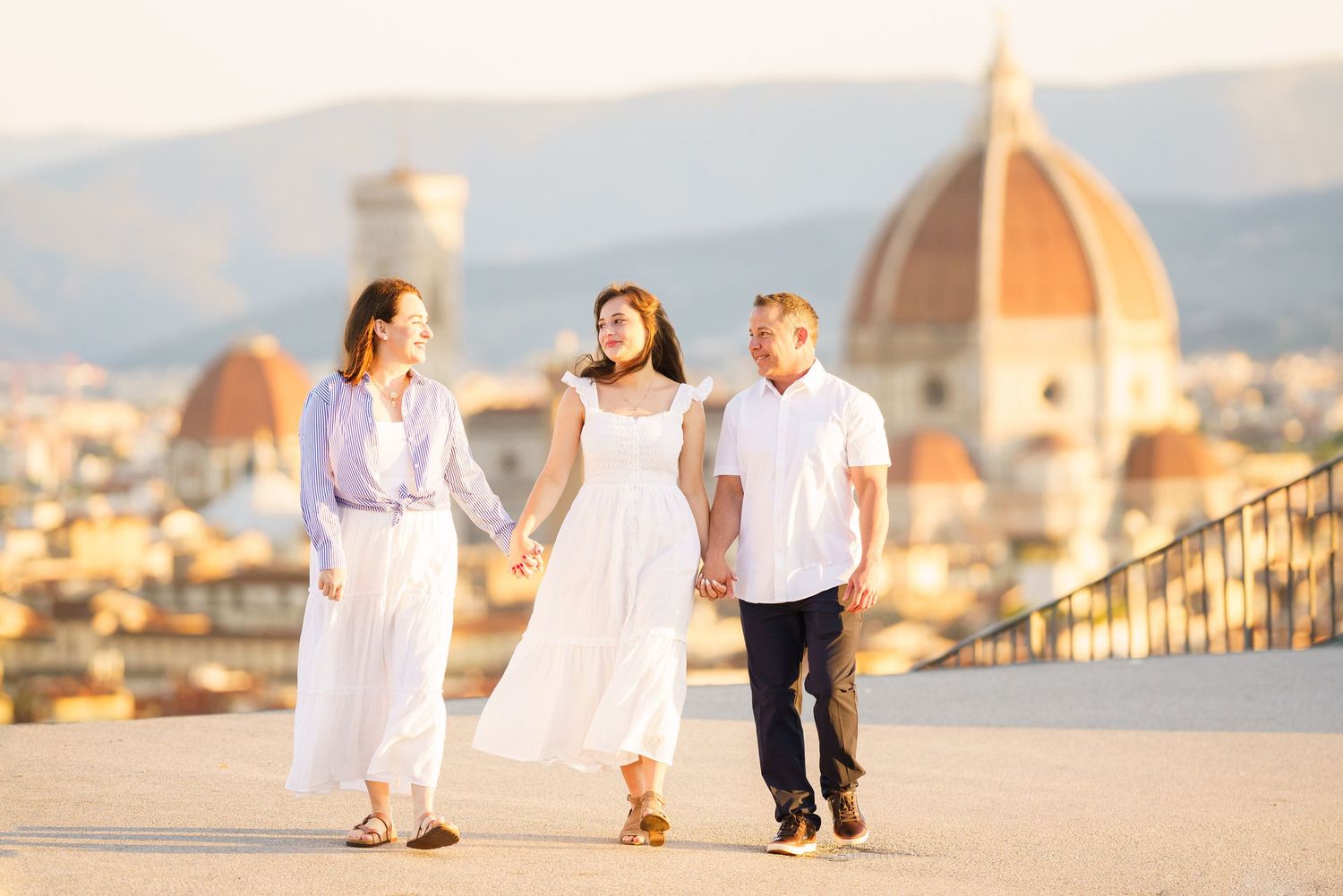 Family walking together in white outfits with Florence Cathedral and cityscape in golden sunset light.