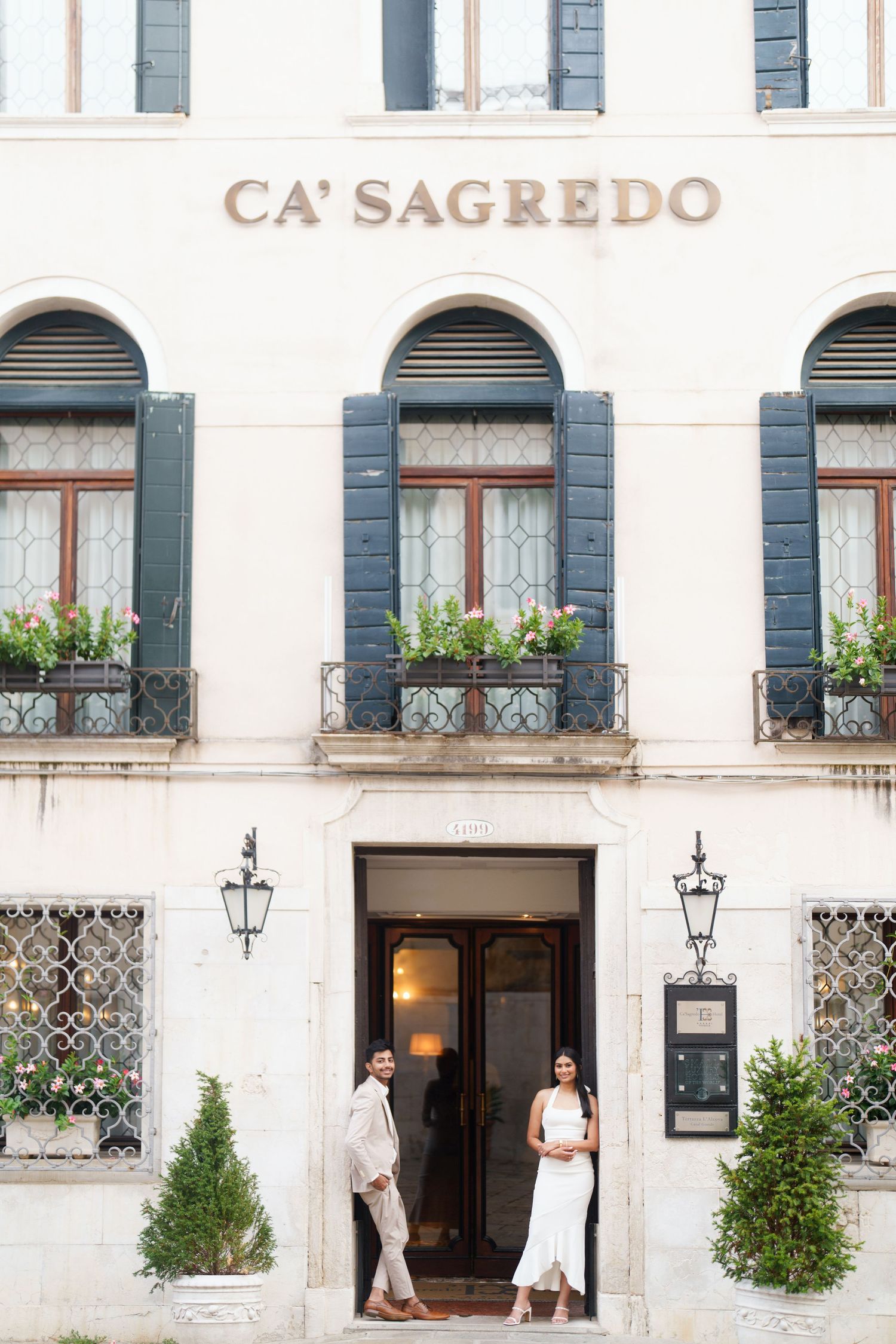 Elegant white facade of Ca' Sagredo hotel in Venice with ornate windows, lanterns, and potted plants along the entrance.