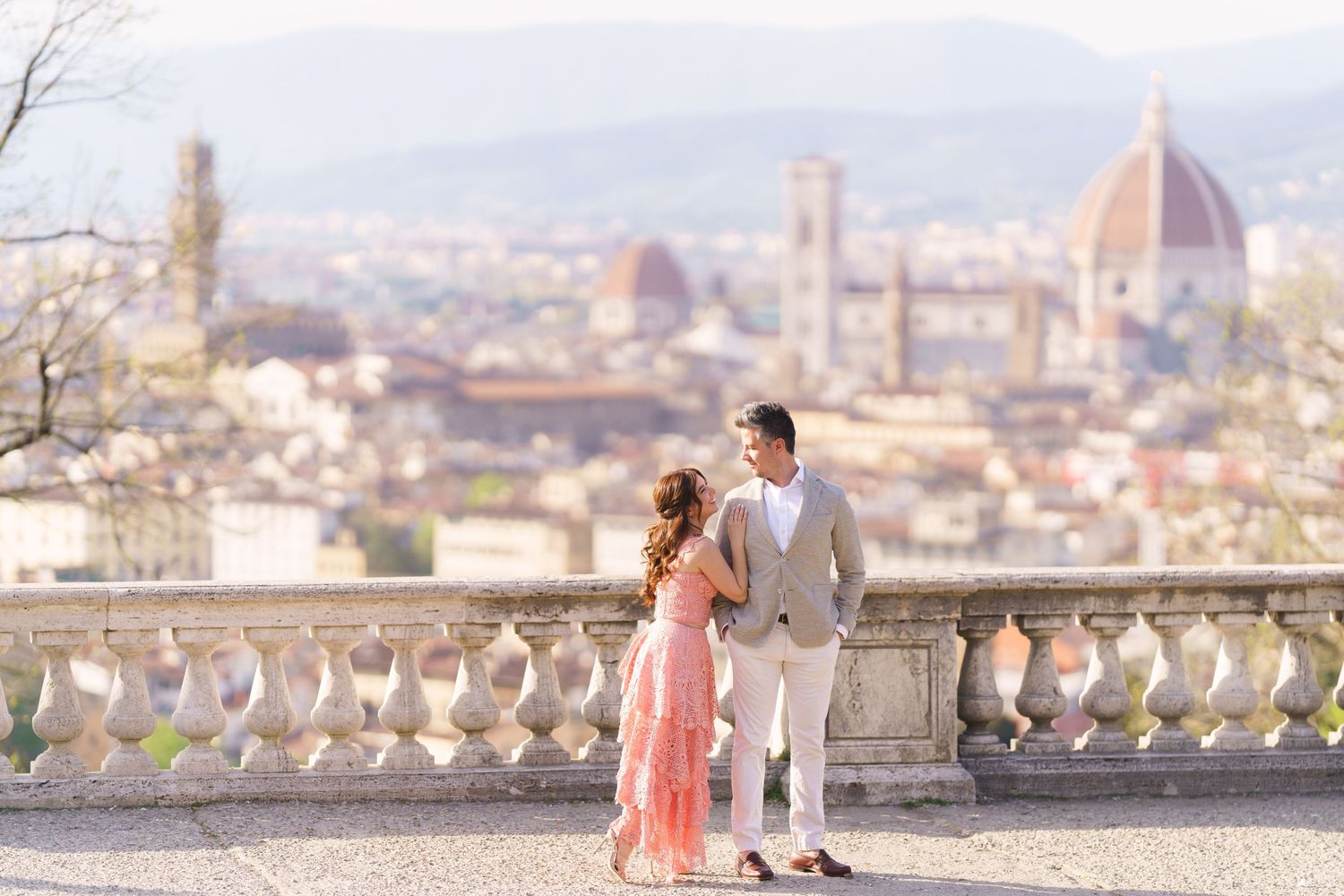 Romantic couple enjoying scenic views of Florence, Italy from a hilltop terrace with the Duomo cathedral in background.
