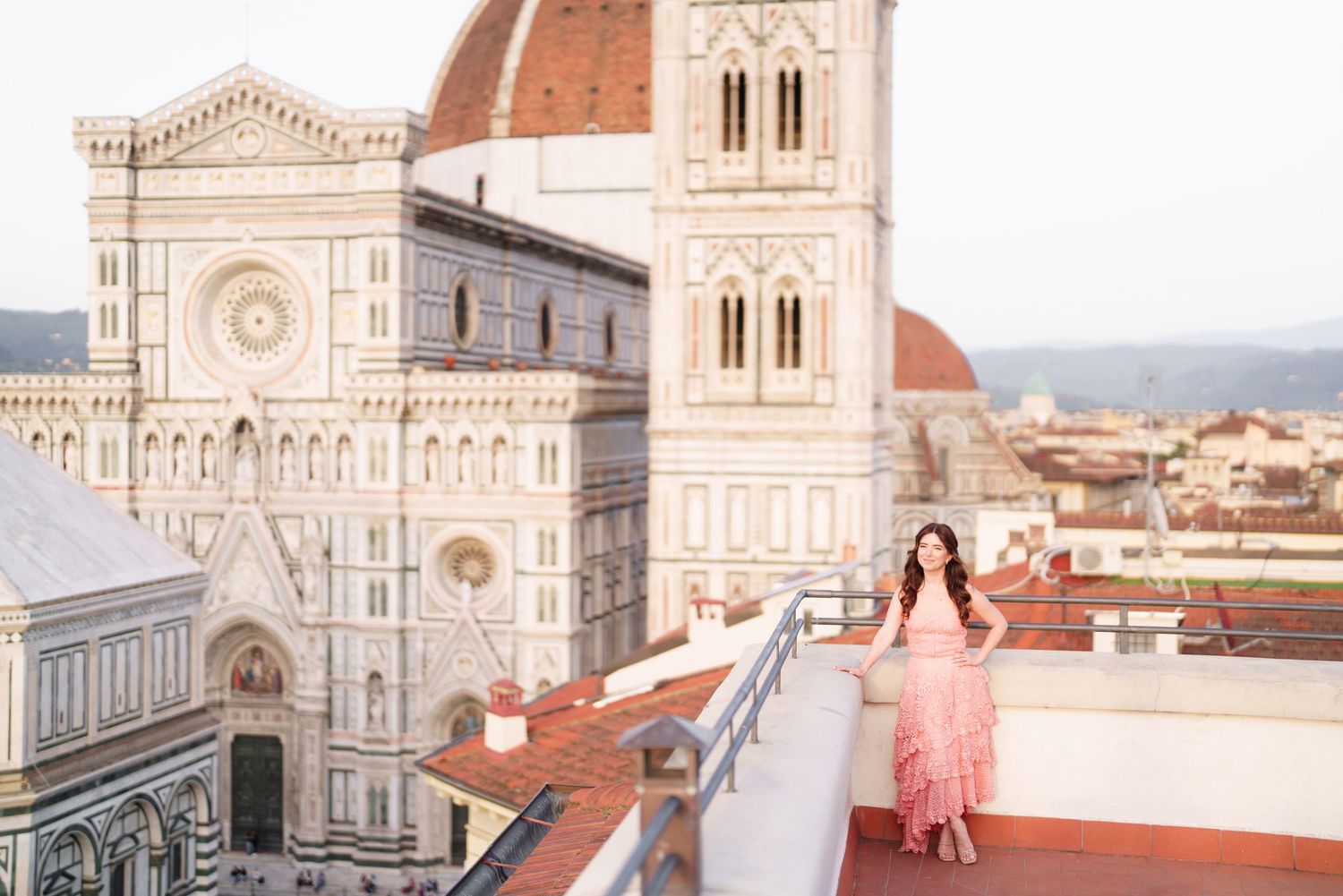 A pink floral dress flows in the wind on a rooftop terrace overlooking Florence Cathedral and its iconic dome in Italy.