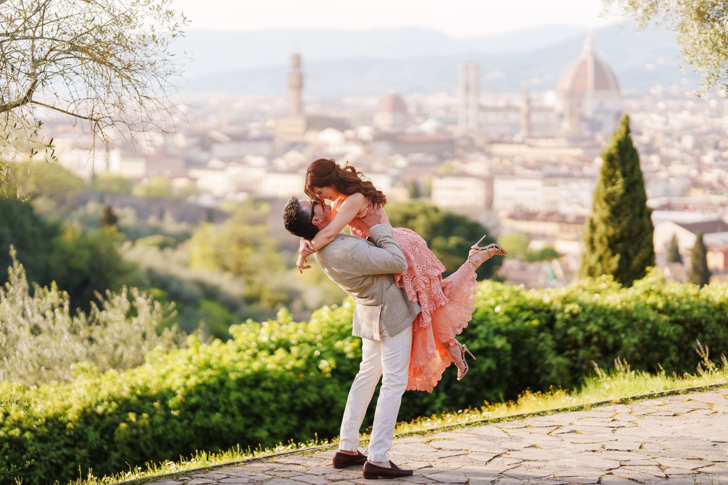 Two people sit on a stone wall overlooking the historic cityscape of Florence, Italy during golden hour.